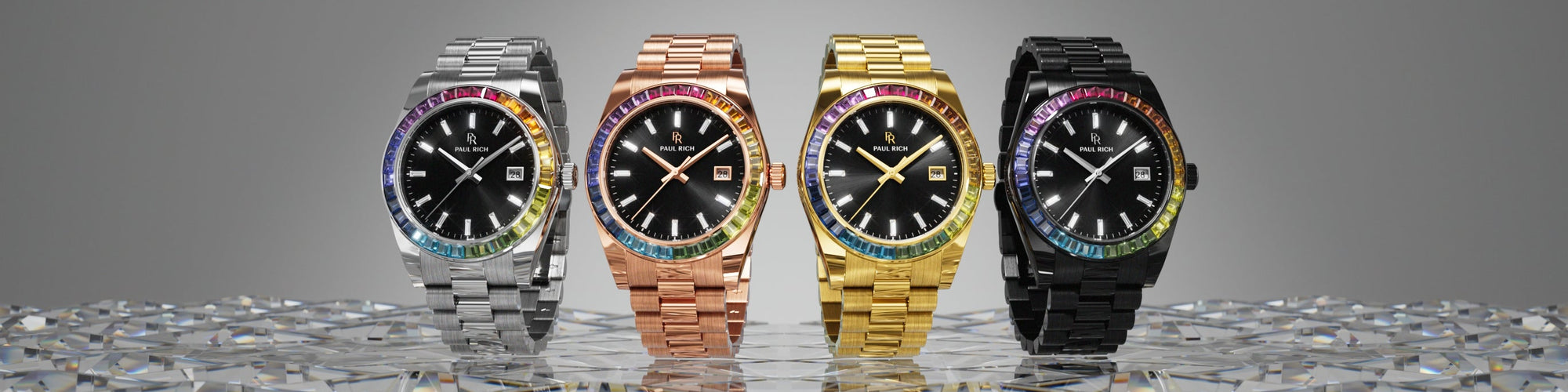Paul Rich rainbow bezel watches in silver, rose gold, yellow gold, and black, displayed on crystal surface with gray gradient background. Paul Rich rainbow bezel watches in silver, rose gold, yellow gold, and black, displayed on crystal surface with gray gradient background.