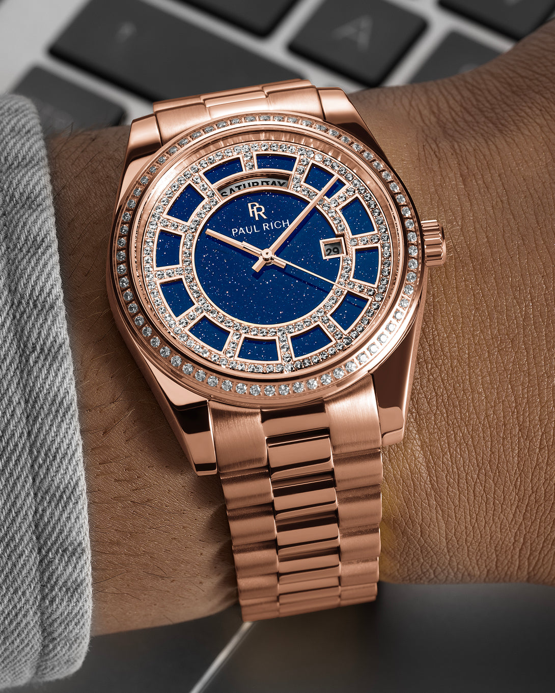 Rose-gold watch with a blue aventurine dial, pavé diamond bezel, and day–date display shown on a wrist with a matching rose-gold bracelet. Rose-gold watch with a blue aventurine dial, pavé diamond bezel, and day–date display shown on a wrist with a matching rose-gold bracelet.