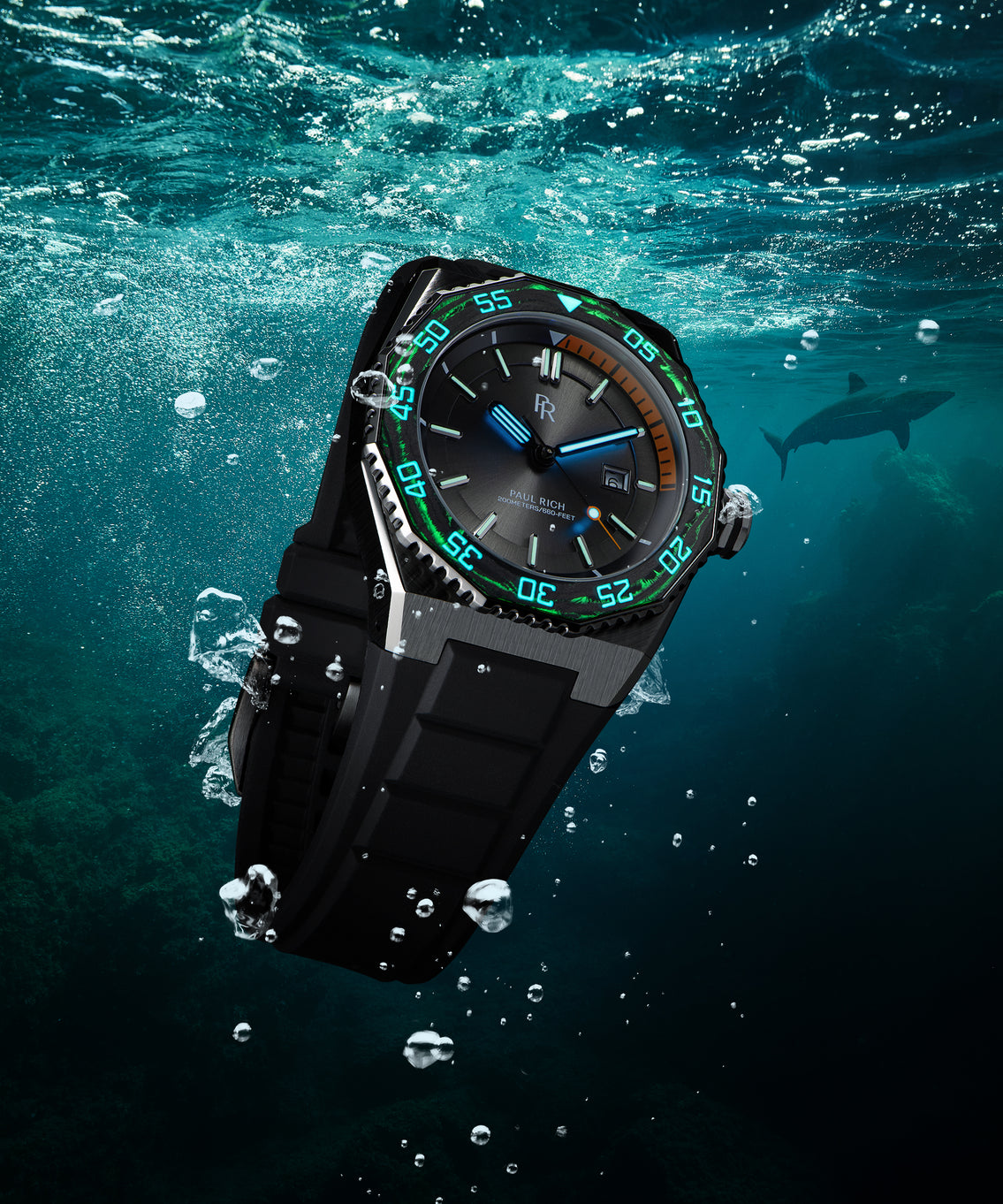 Paul Rich dive watch underwater with glowing blue hands and green bezel lume, orange dive timer, and a shark visible in the distance. Paul Rich dive watch underwater with glowing blue hands and green bezel lume, orange dive timer, and a shark visible in the distance.
