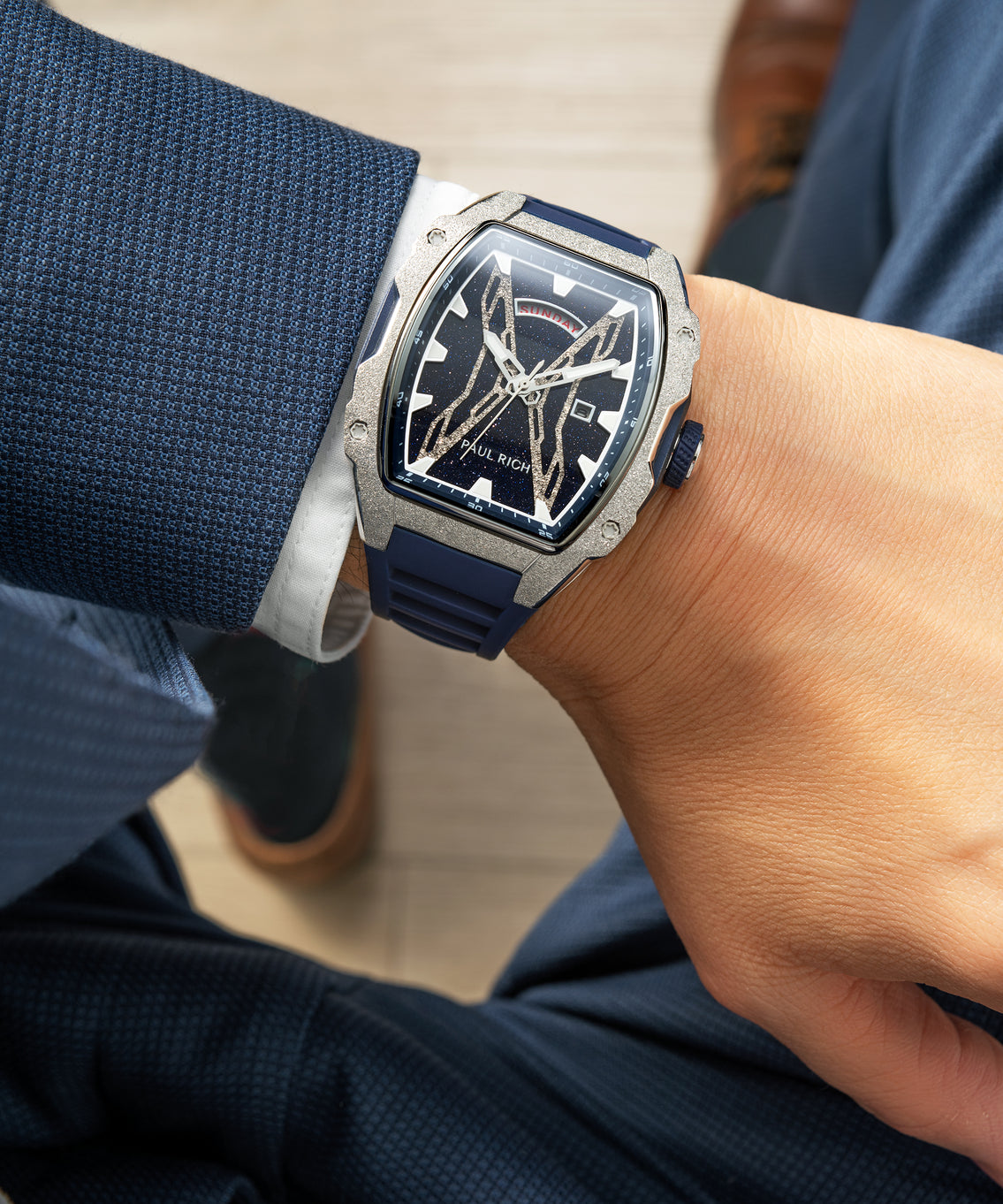 Paul Rich watch with blue aventurine dial, silver frosted bezel, and blue strap worn on wrist with textured navy suit and white cuff. Paul Rich watch with blue aventurine dial, silver frosted bezel, and blue strap worn on wrist with textured navy suit and white cuff.