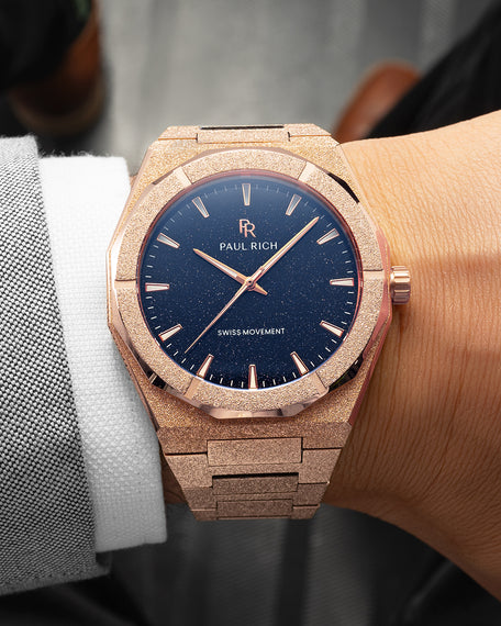 Frosted Star Dust II Rose Gold Rose gold watch with shimmering frosted case and blue aventurine dial, worn with a white cuff and grey suit in formal setting.