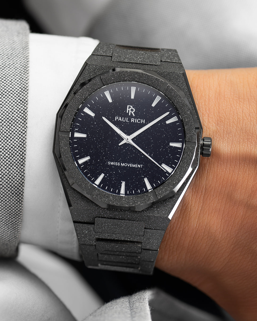 Paul Rich watch with frosted black case and black aventurine dial, worn on wrist with a white cuff and light grey textured suit. Paul Rich watch with frosted black case and black aventurine dial, worn on wrist with a white cuff and light grey textured suit.