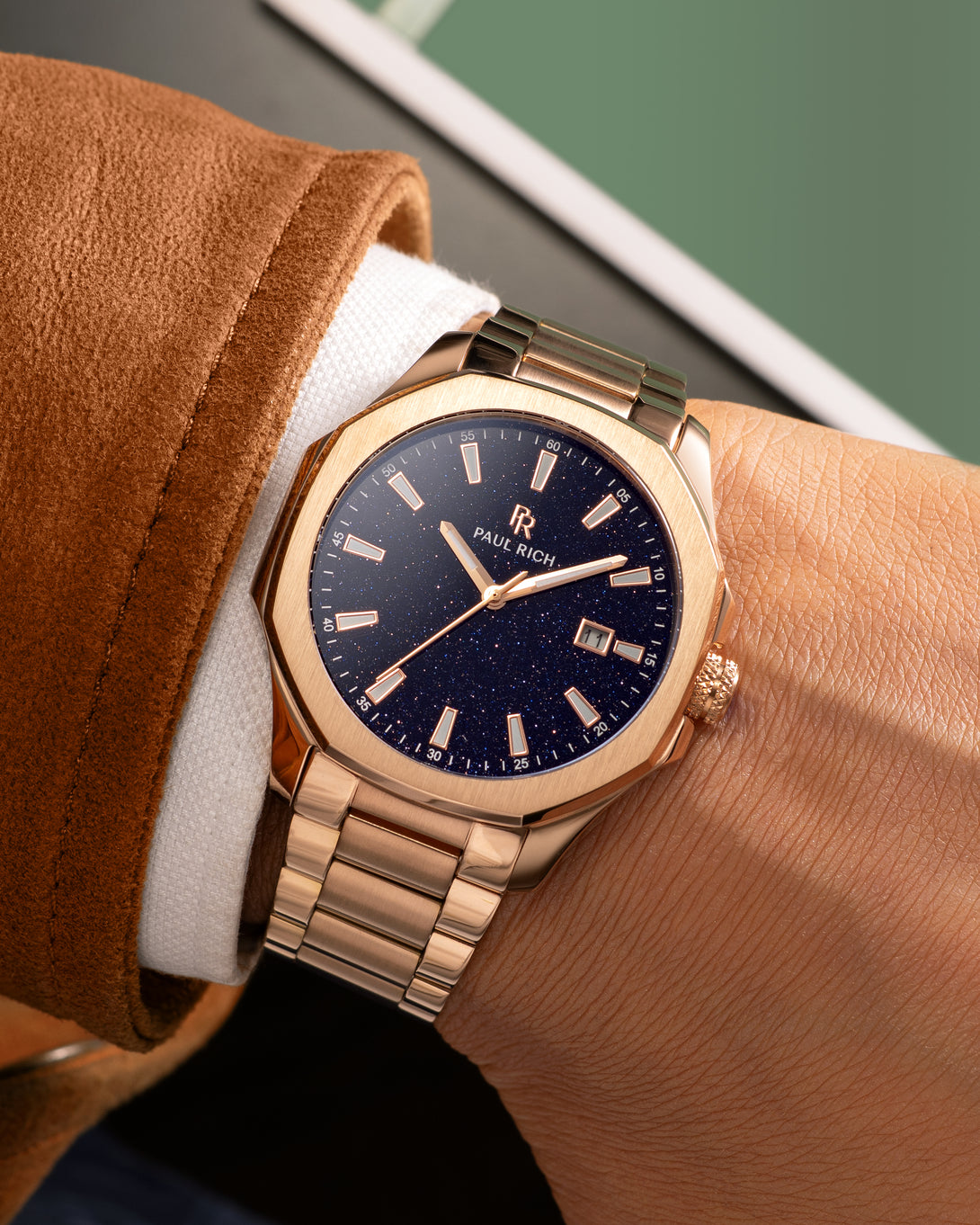 Rose gold Paul Rich watch with blue aventurine dial and date window, worn on wrist with white cuff and brown suede jacket. Rose gold Paul Rich watch with blue aventurine dial and date window, worn on wrist with white cuff and brown suede jacket.