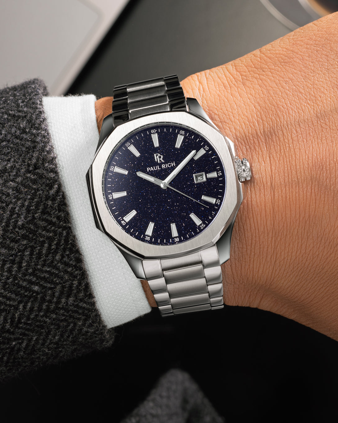 Silver Paul Rich watch with blue aventurine dial and date window, worn on wrist with white shirt and dark herringbone-patterned coat. Silver Paul Rich watch with blue aventurine dial and date window, worn on wrist with white shirt and dark herringbone-patterned coat.
