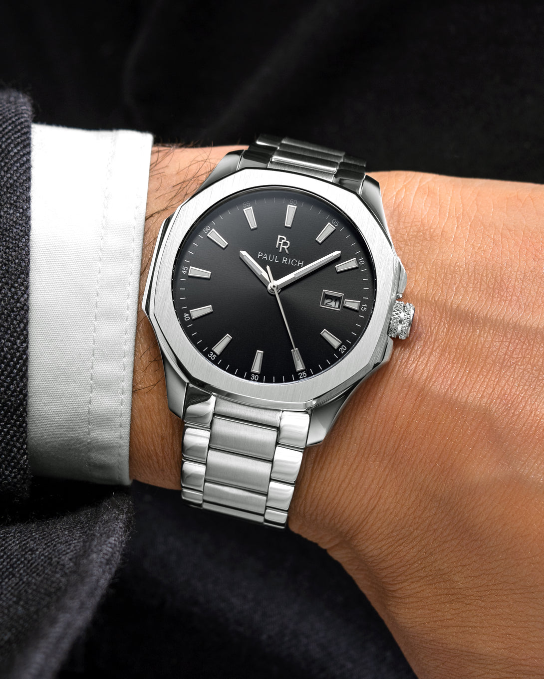 Silver Paul Rich watch with black sunray dial, steel bracelet, date window, and bold markers on a suited man's wrist. Silver Paul Rich watch with black sunray dial, steel bracelet, date window, and bold markers on a suited man's wrist.