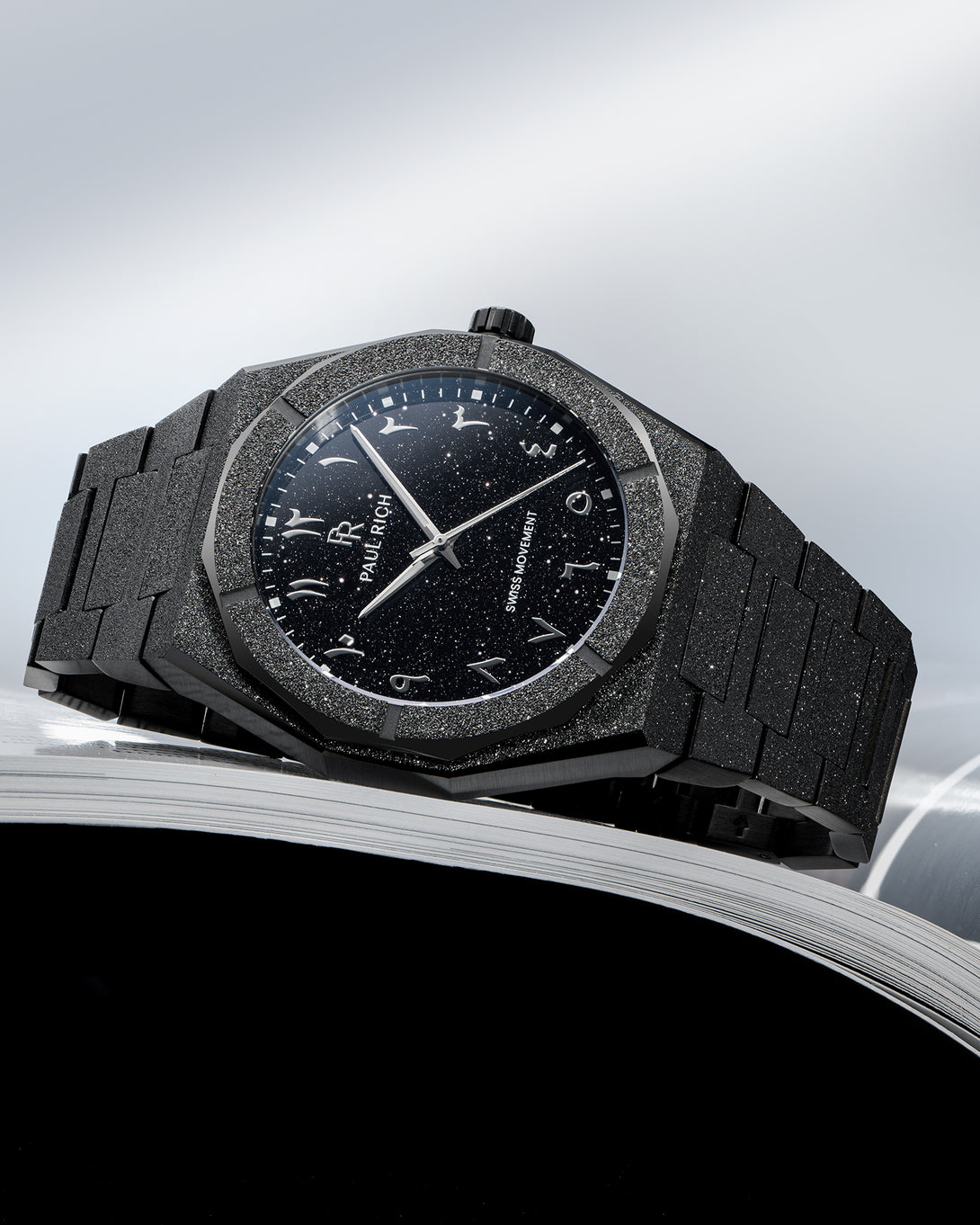 Paul Rich frosted black watch with black aventurine dial and silver Arabic numerals, displayed on the edge of an open magazine. Paul Rich frosted black watch with black aventurine dial and silver Arabic numerals, displayed on the edge of an open magazine.