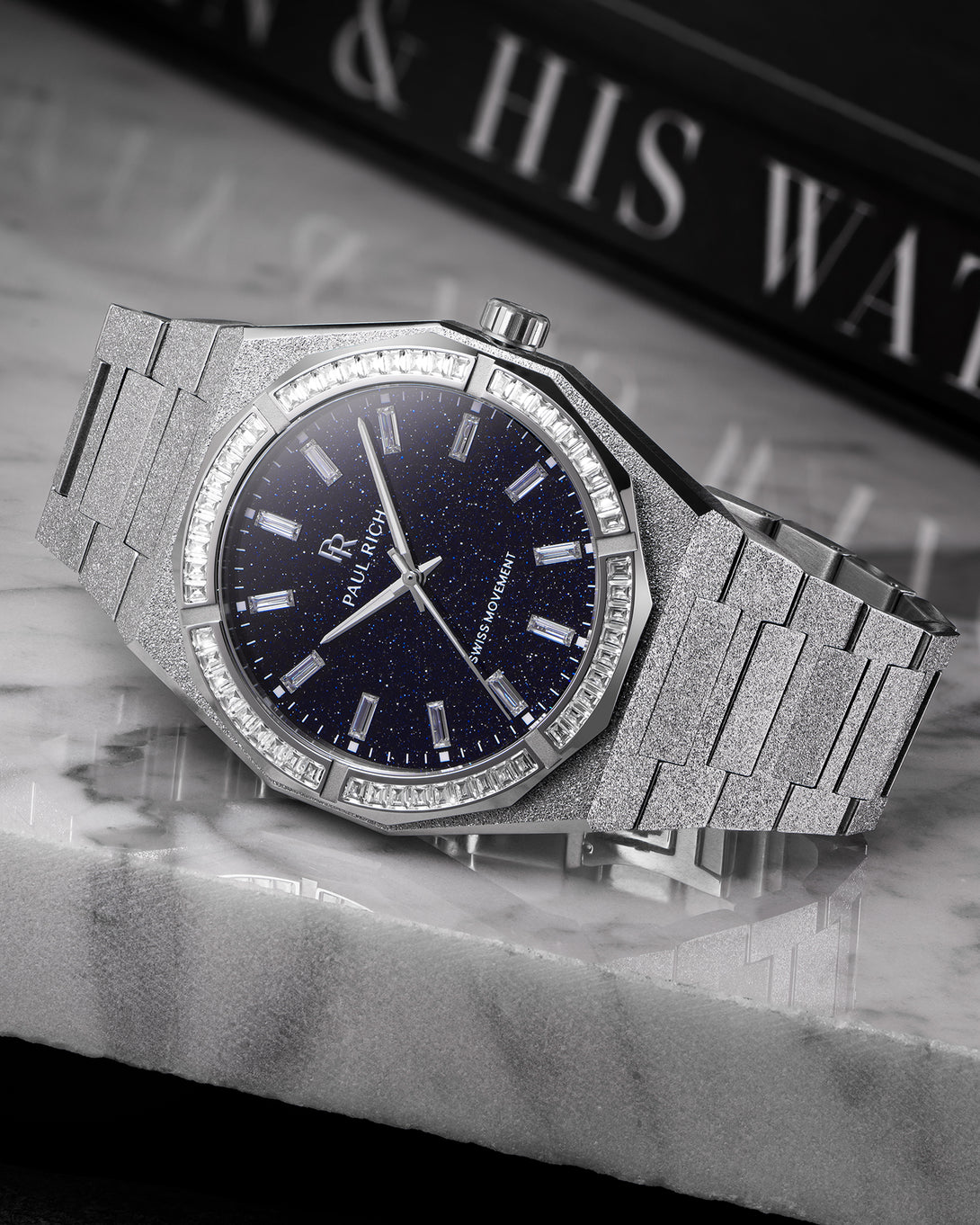 Silver frosted watch with aventurine dial and baguette-cut moissanite bezel, displayed on a polished marble surface. Silver frosted watch with aventurine dial and baguette-cut moissanite bezel, displayed on a polished marble surface.