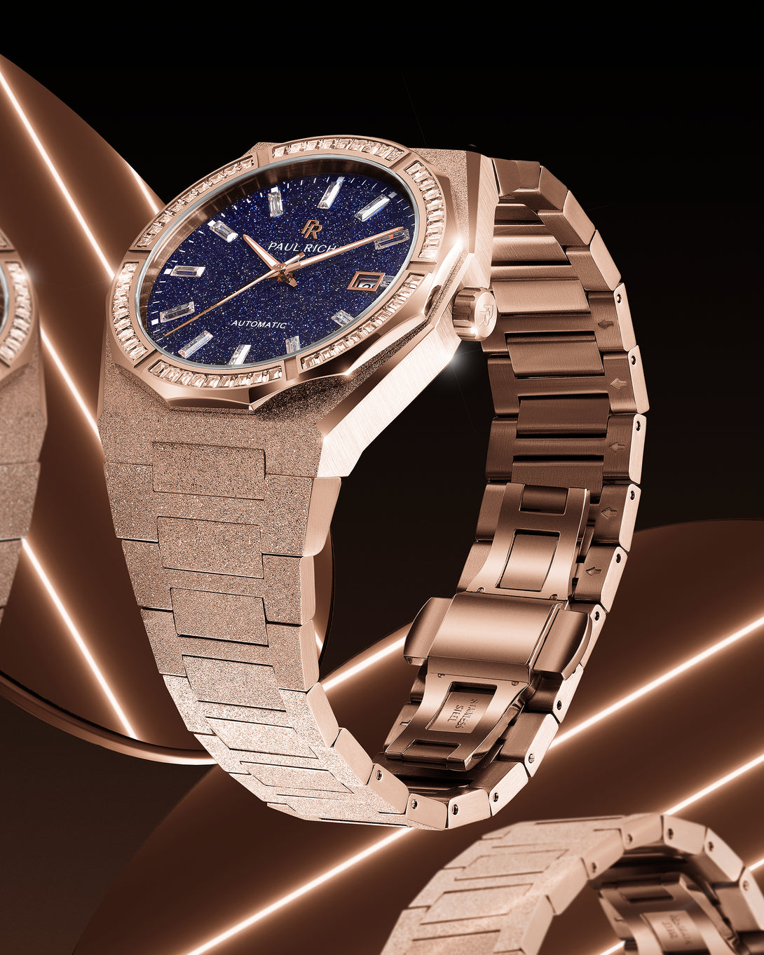 Side view of a rose gold Paul Rich watch with frosted bracelet and blue aventurine dial, reflecting warm light across a mirrored surface. Side view of a rose gold Paul Rich watch with frosted bracelet and blue aventurine dial, reflecting warm light across a mirrored surface.