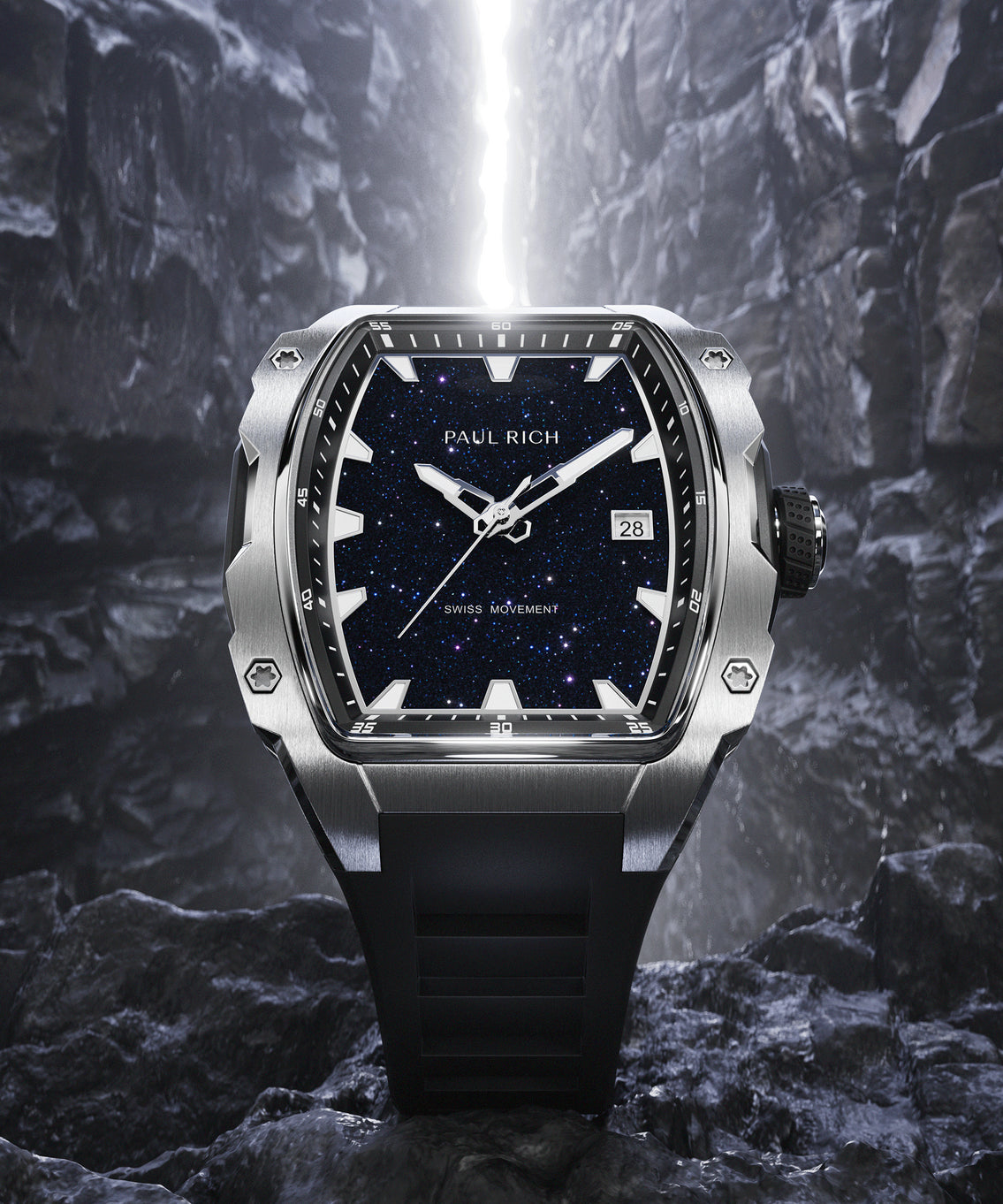 Paul Rich silver-tonneau watch with blue aventurine dial, silver hands, and black strap displayed on rugged rock with light beam in background. Paul Rich silver-tonneau watch with blue aventurine dial, silver hands, and black strap displayed on rugged rock with light beam in background.
