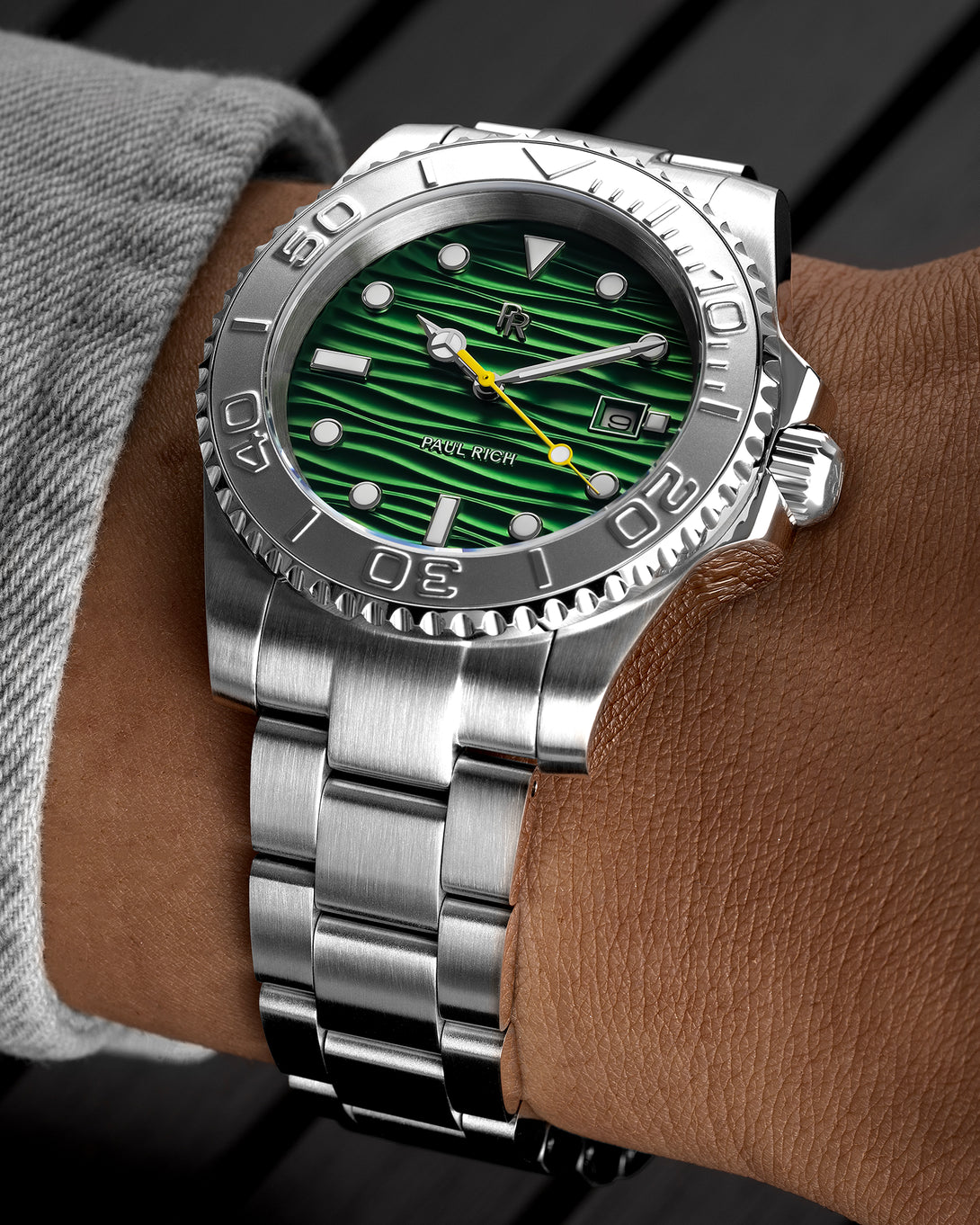 Stainless steel watch with a green wave-textured dial and yellow seconds hand shown on a wrist, highlighting the bezel, markers, and brushed bracelet. Stainless steel watch with a green wave-textured dial and yellow seconds hand shown on a wrist, highlighting the bezel, markers, and brushed bracelet.