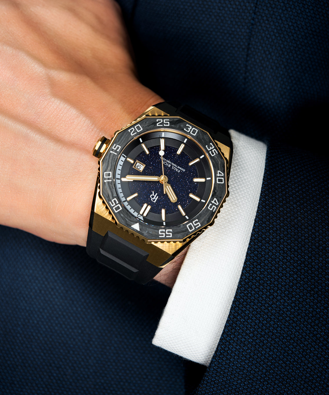 Paul Rich dive watch with gold case and aventurine dial worn on wrist, paired with white cuff and navy textured suit jacket. Paul Rich dive watch with gold case and aventurine dial worn on wrist, paired with white cuff and navy textured suit jacket.