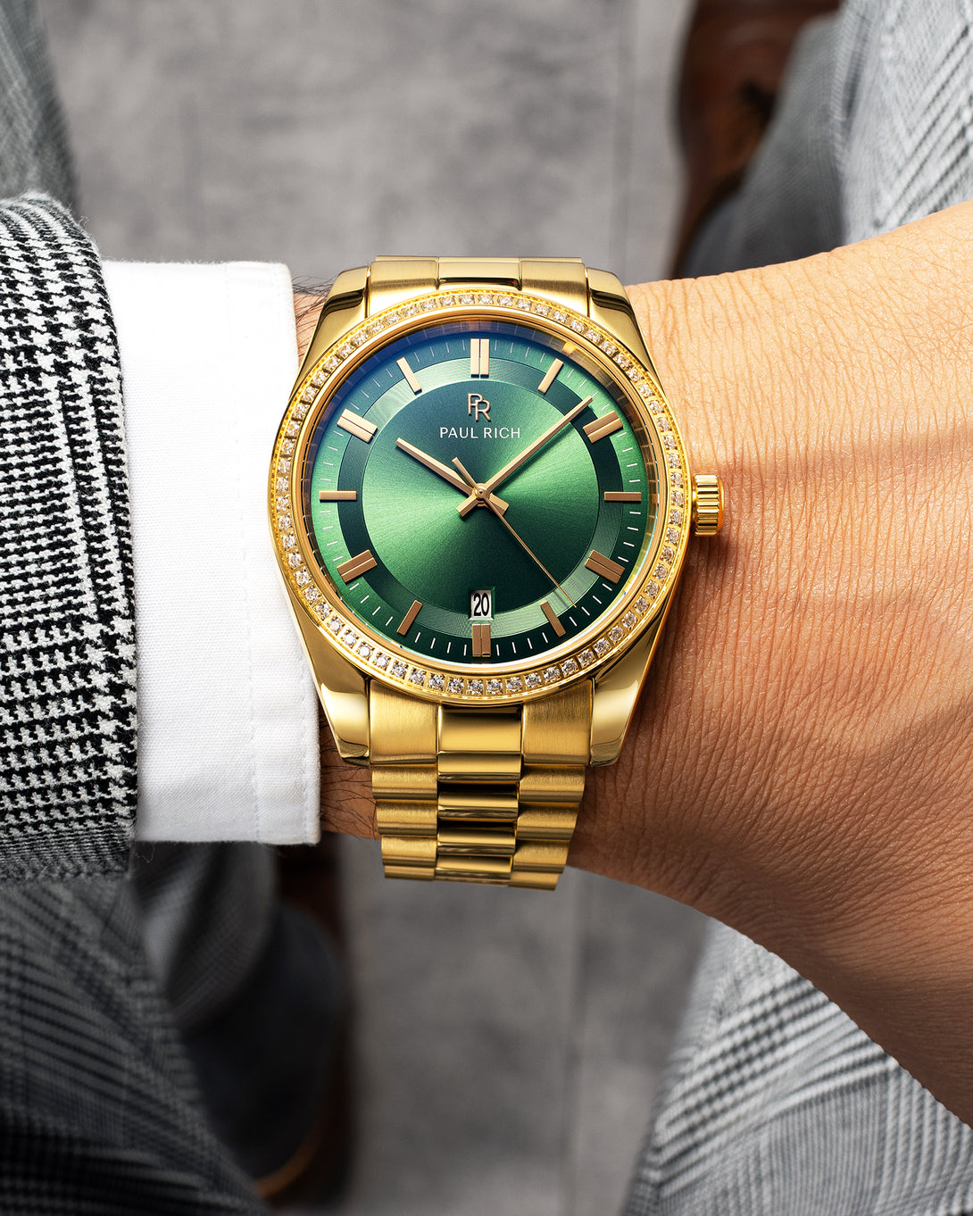 Gold-tone Paul Rich watch with green sunray dial, diamond-set bezel, and gold link bracelet, worn on wrist with a white shirt and black-and-white check blazer. Gold-tone Paul Rich watch with green sunray dial, diamond-set bezel, and gold link bracelet, worn on wrist with a white shirt and black-and-white check blazer.