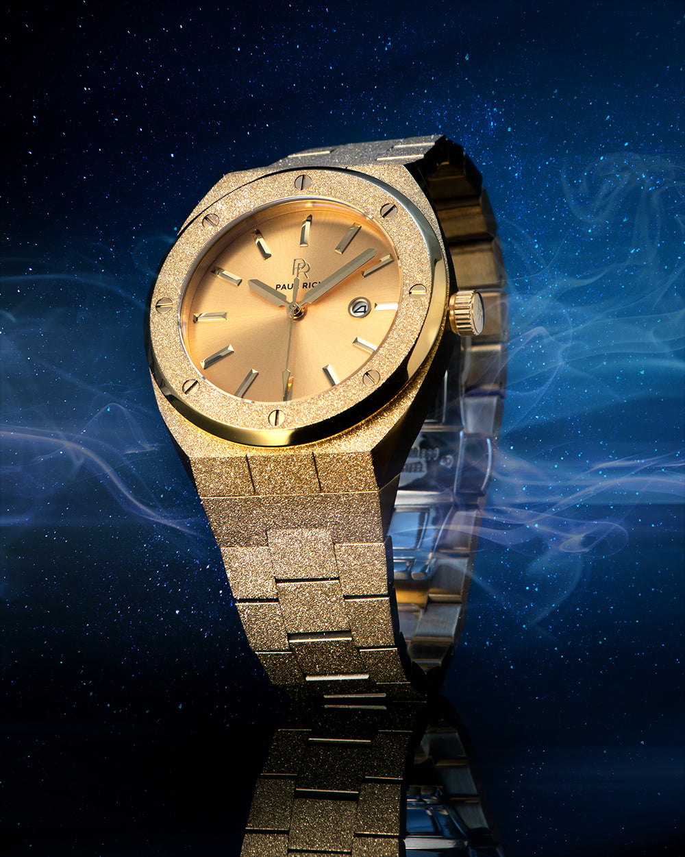 Paul Rich watch with frosted gold case and bracelet, metallic champagne gold sunray dial, and date window, displayed against a starry night sky with mist. Paul Rich watch with frosted gold case and bracelet, metallic champagne gold sunray dial, and date window, displayed against a starry night sky with mist.