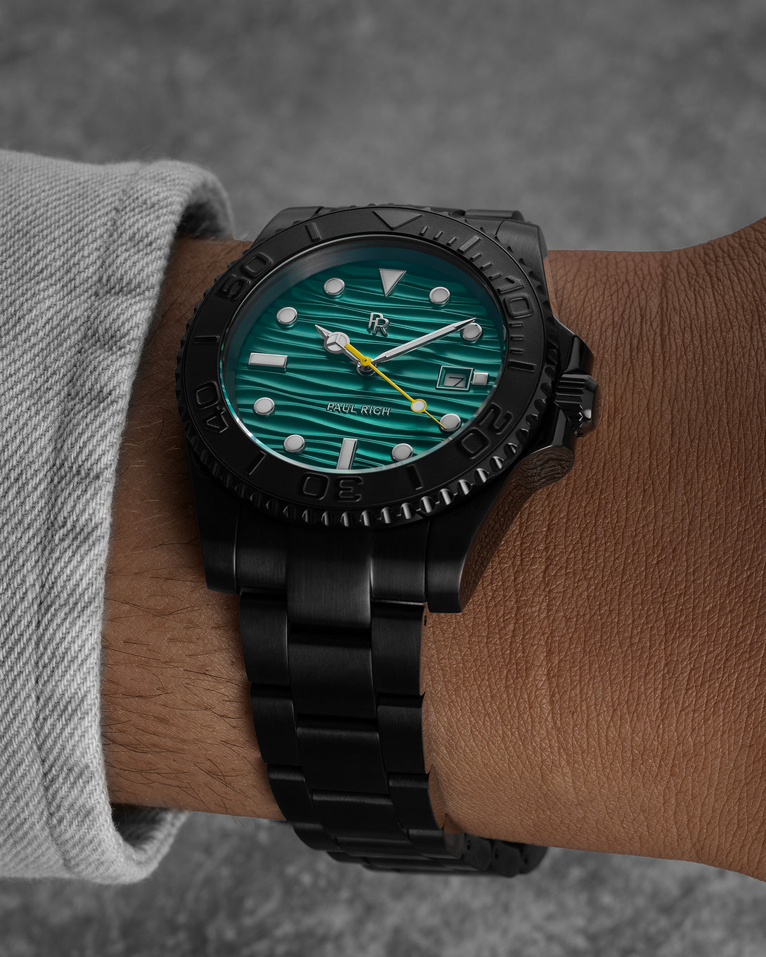 Black stainless steel watch with a teal wave-textured dial shown on a wrist, highlighting the bracelet, bezel, luminous markers, and yellow seconds hand. Black stainless steel watch with a teal wave-textured dial shown on a wrist, highlighting the bracelet, bezel, luminous markers, and yellow seconds hand.