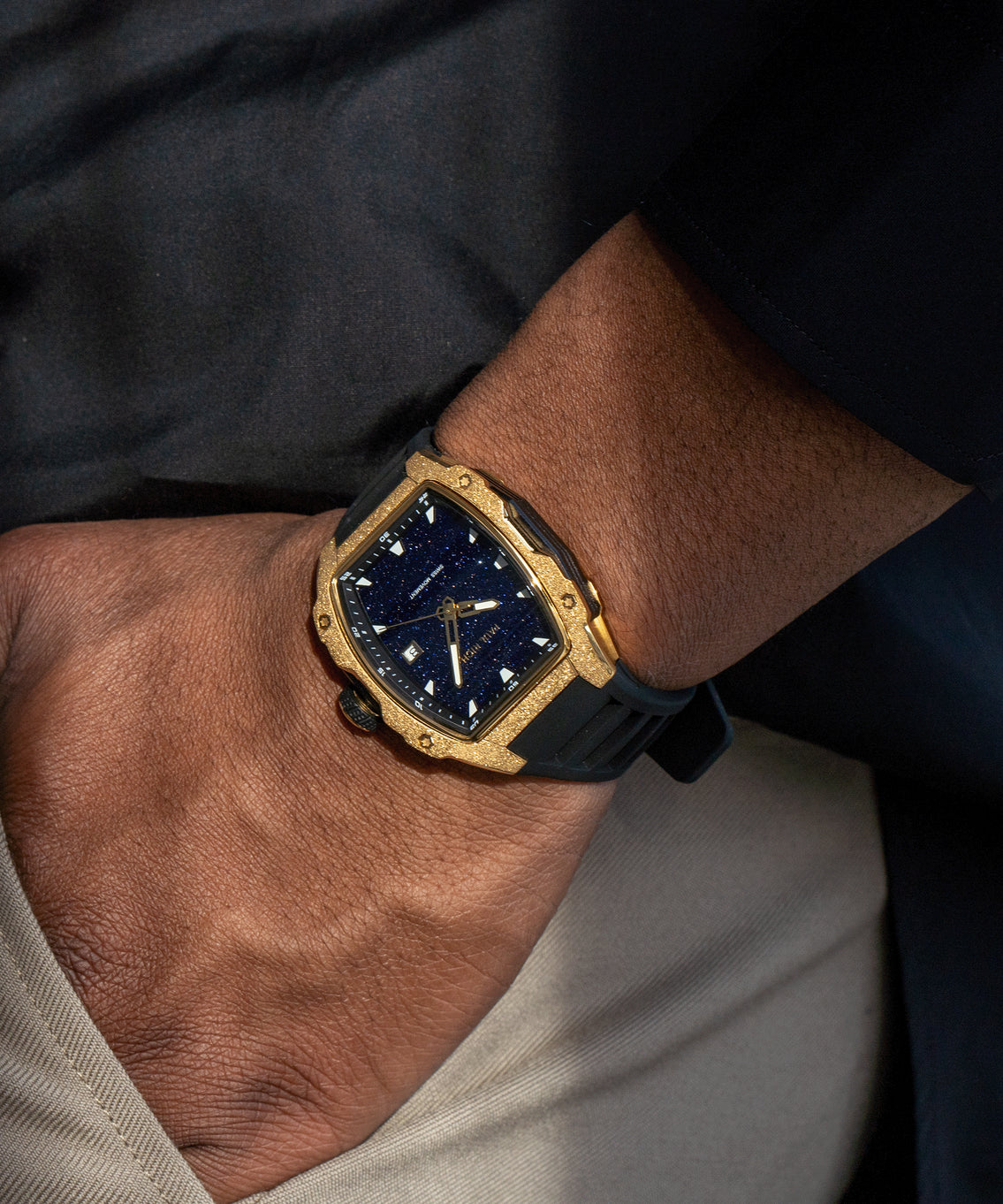 Tonneau-shaped Paul Rich watch with blue aventurine dial and gold frosted bezel worn on wrist, paired with beige pants and black top. Tonneau-shaped Paul Rich watch with blue aventurine dial and gold frosted bezel worn on wrist, paired with beige pants and black top.