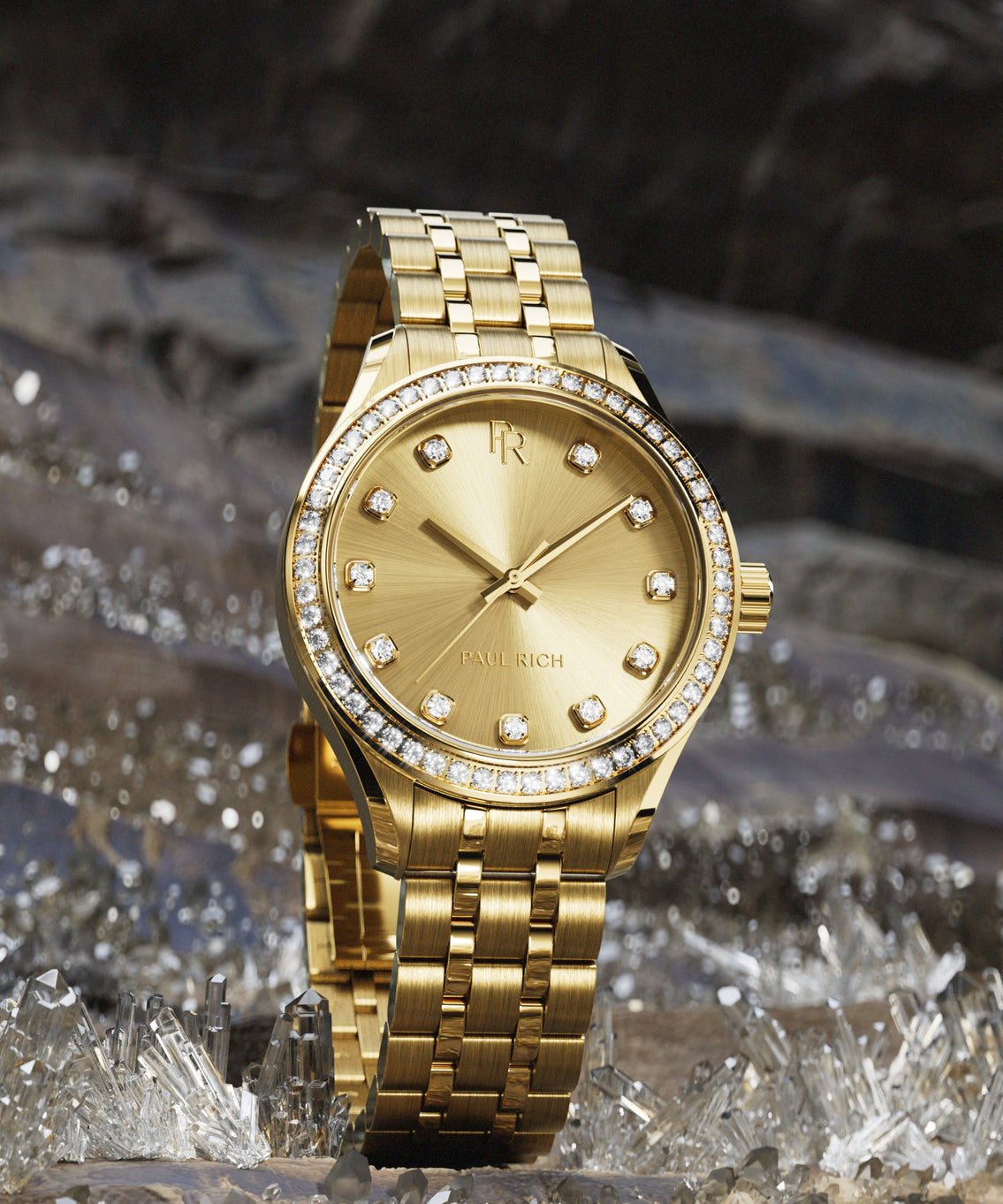 Gold-tone Paul Rich watch with sunray gold dial, diamond hour markers, and gem-set bezel, displayed upright on a bed of clear crystals. Gold-tone Paul Rich watch with sunray gold dial, diamond hour markers, and gem-set bezel, displayed upright on a bed of clear crystals.