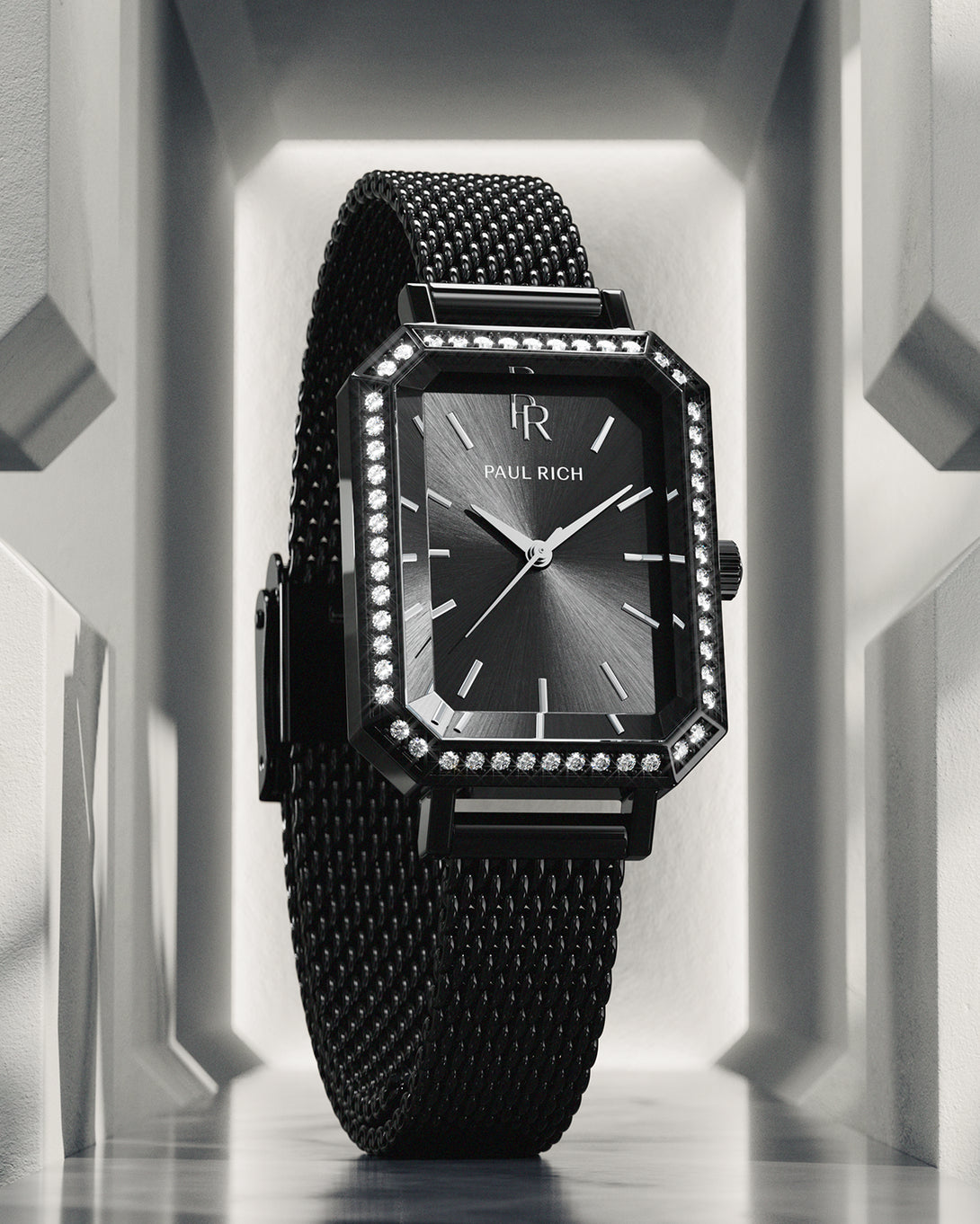 Black Paul Rich watch with black sunray dial, gem-set octagonal bezel, and black mesh strap, displayed upright in a geometric white architectural setting with dramatic lighting. Black Paul Rich watch with black sunray dial, gem-set octagonal bezel, and black mesh strap, displayed upright in a geometric white architectural setting with dramatic lighting.
