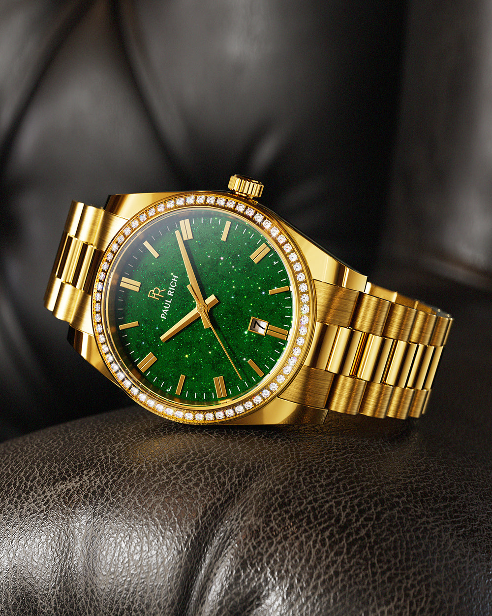 Gold-tone Paul Rich watch with green aventurine dial, diamond-set bezel, and gold link bracelet, displayed resting on a dark brown leather cushion. Gold-tone Paul Rich watch with green aventurine dial, diamond-set bezel, and gold link bracelet, displayed resting on a dark brown leather cushion.