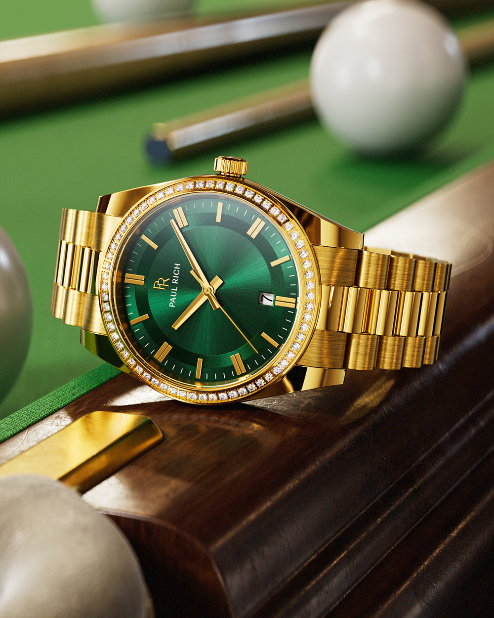 Gold-tone Paul Rich watch with green sunray dial, diamond-set bezel, and gold link bracelet, displayed on the wooden edge of a pool table with billiard balls and cues in the background. Gold-tone Paul Rich watch with green sunray dial, diamond-set bezel, and gold link bracelet, displayed on the wooden edge of a pool table with billiard balls and cues in the background.