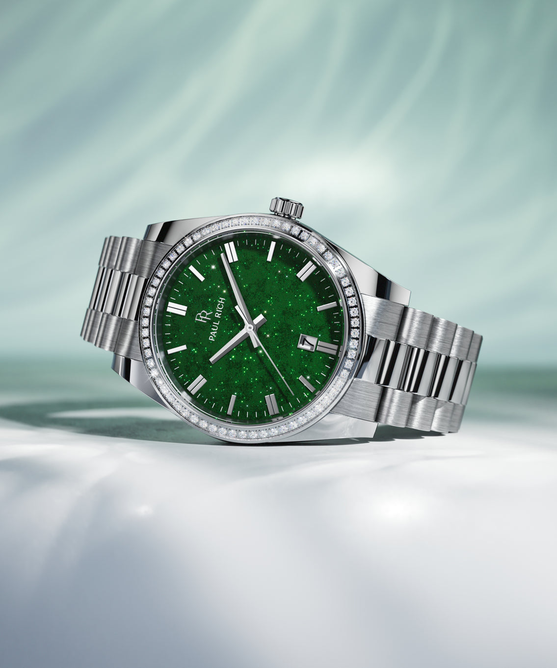 Silver wristwatch with a green aventurine dial, crystal-set bezel, and metal bracelet displayed on a white surface with soft green lighting. Silver wristwatch with a green aventurine dial, crystal-set bezel, and metal bracelet displayed on a white surface with soft green lighting.