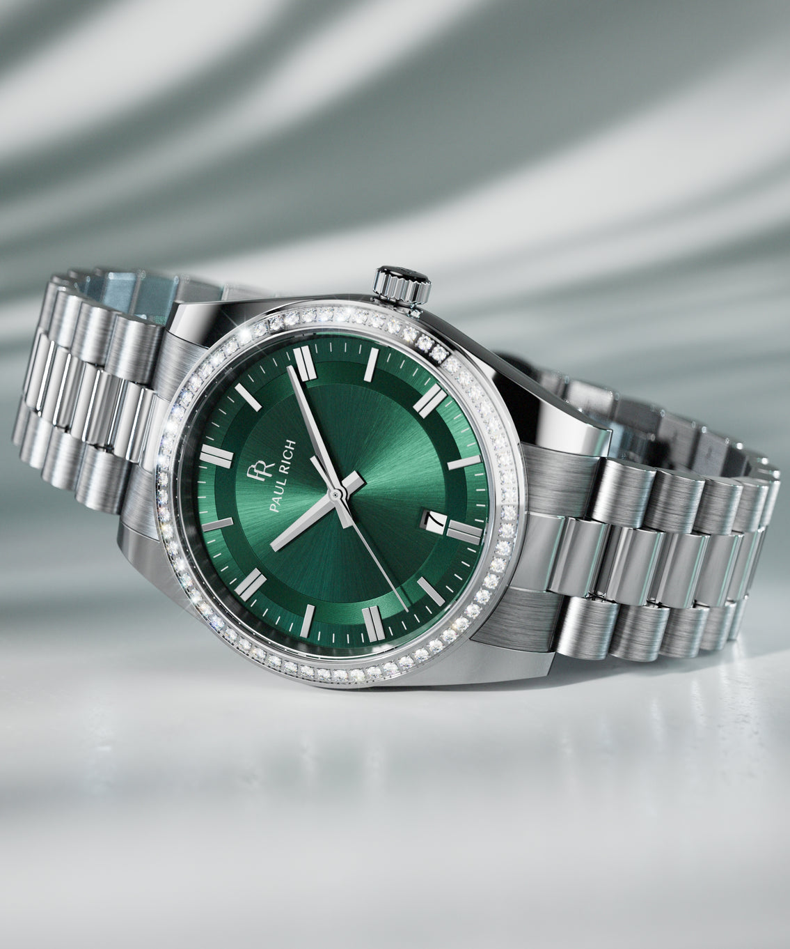 Silver wristwatch with a green sunburst dial, crystal-set bezel, and metal bracelet displayed on a reflective surface with soft lighting. Silver wristwatch with a green sunburst dial, crystal-set bezel, and metal bracelet displayed on a reflective surface with soft lighting.