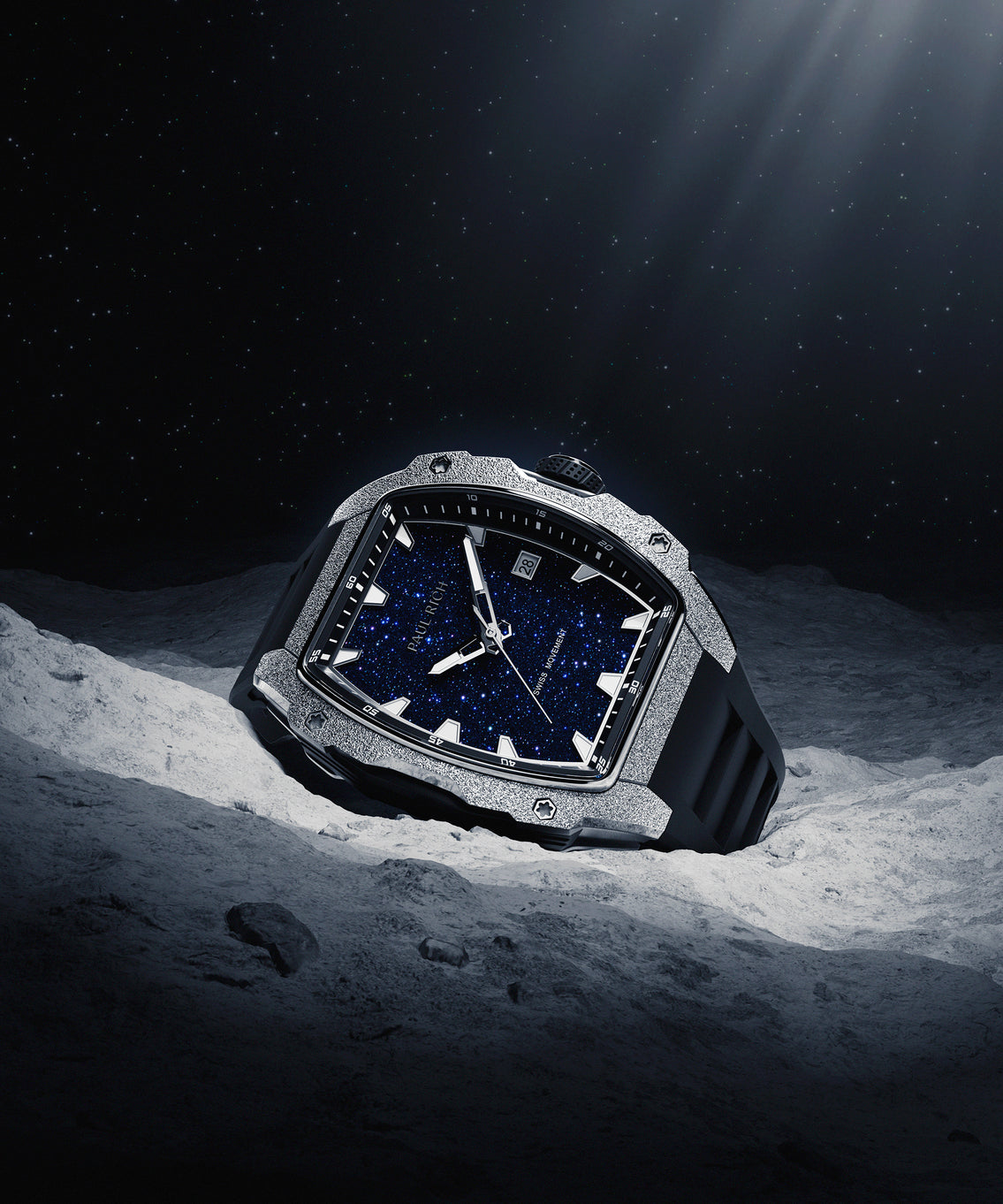 Paul Rich watch with tonneau case, frosted silver bezel, blue aventurine dial, and black rubber strap, displayed on moon-like surface under starlight. Paul Rich watch with tonneau case, frosted silver bezel, blue aventurine dial, and black rubber strap, displayed on moon-like surface under starlight.