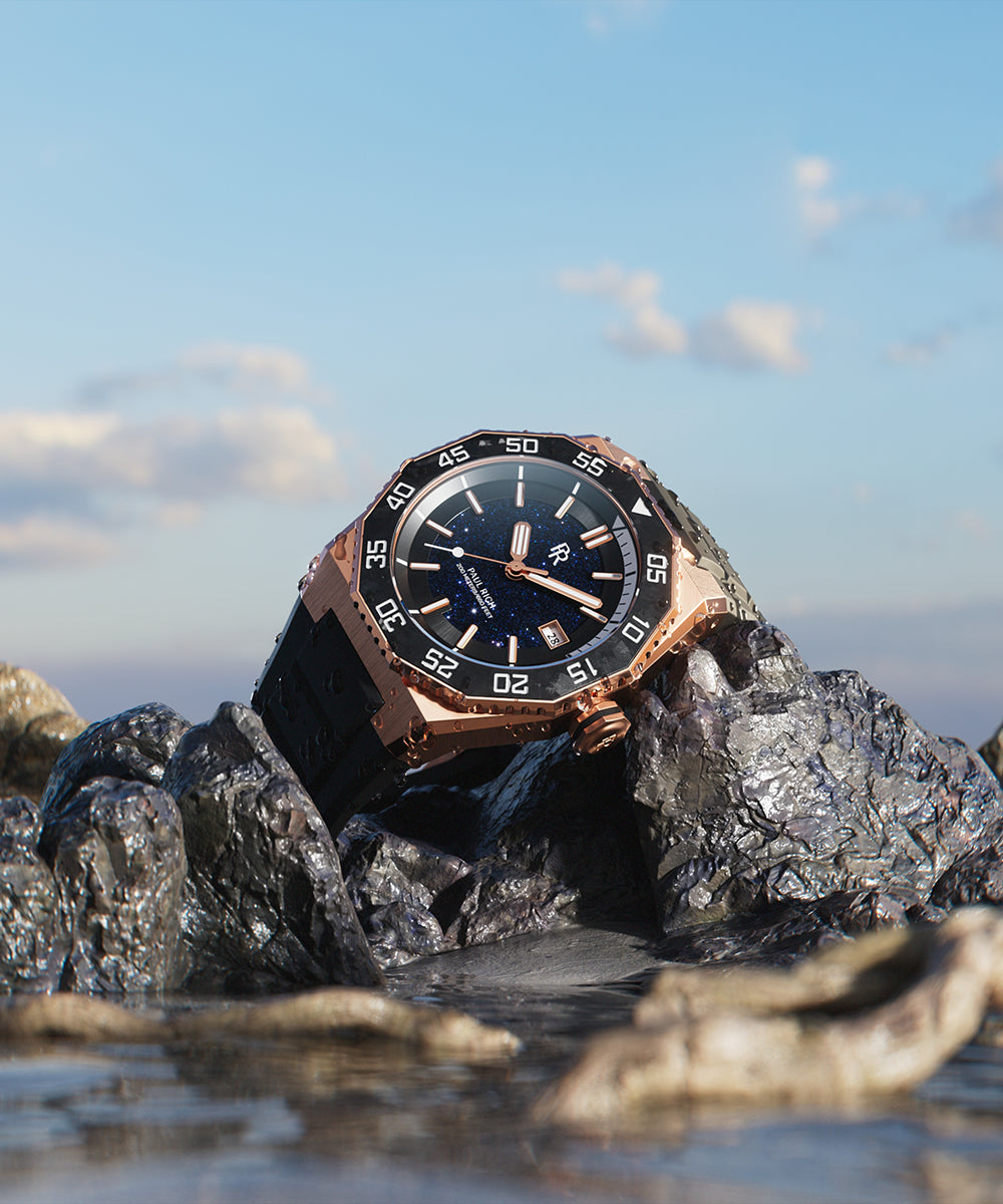 Paul Rich watch with rose gold case and blue aventurine dial resting on wet rocks by the ocean, with a blue sky and clouds in the background. Paul Rich watch with rose gold case and blue aventurine dial resting on wet rocks by the ocean, with a blue sky and clouds in the background.