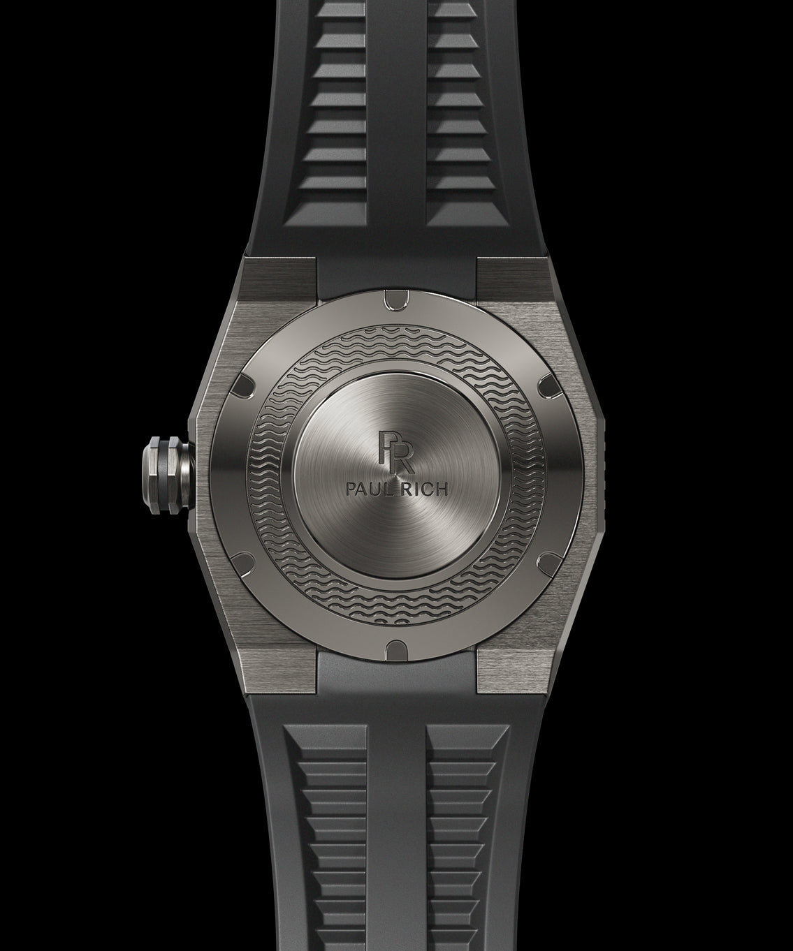 Back view of a Paul Rich dive watch with silver brushed steel caseback, engraved wave pattern, and black rubber strap. Back view of a Paul Rich dive watch with silver brushed steel caseback, engraved wave pattern, and black rubber strap.