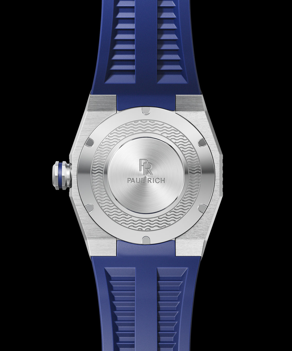 Caseback view of a diver-style watch with brushed steel finish, engraved Paul Rich logo, wave pattern detailing, and blue rubber strap. Caseback view of a diver-style watch with brushed steel finish, engraved Paul Rich logo, wave pattern detailing, and blue rubber strap.