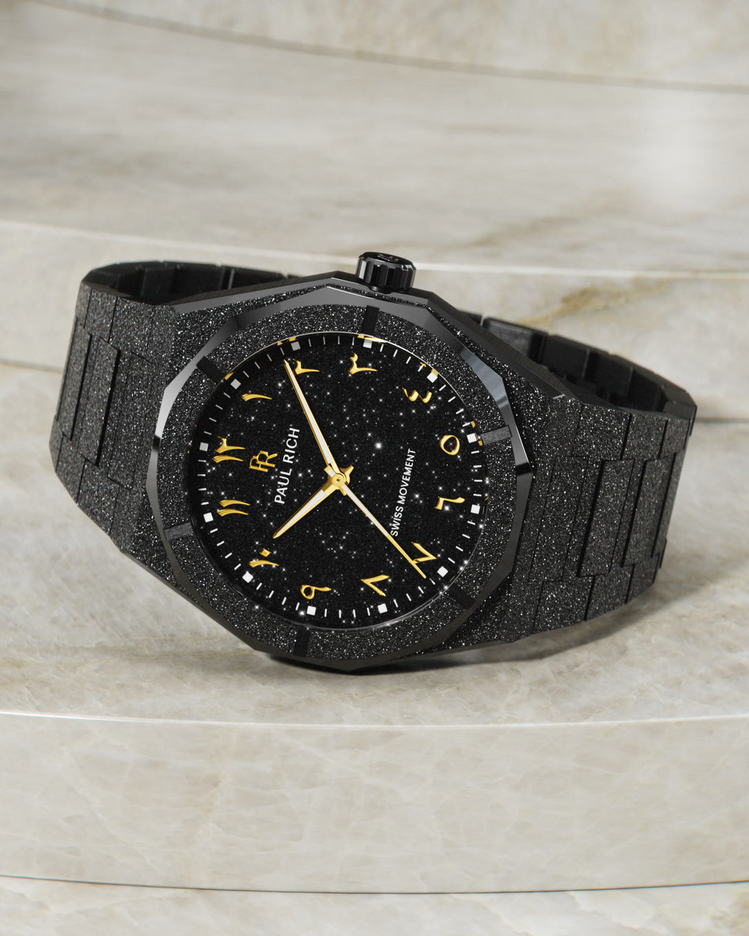 Paul Rich frosted black watch with gold Arabic numerals and black aventurine dial, displayed on light marble-textured stone steps. Paul Rich frosted black watch with gold Arabic numerals and black aventurine dial, displayed on light marble-textured stone steps.