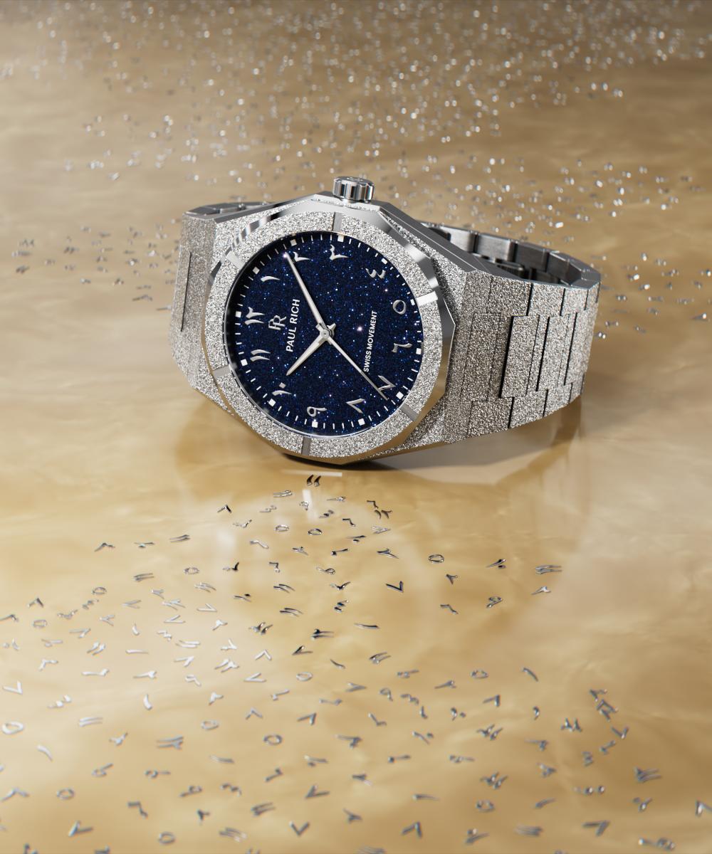 Paul Rich frosted silver watch with blue aventurine dial and Eastern Arabic numerals, displayed on a golden surface with scattered letters. Paul Rich frosted silver watch with blue aventurine dial and Eastern Arabic numerals, displayed on a golden surface with scattered letters.