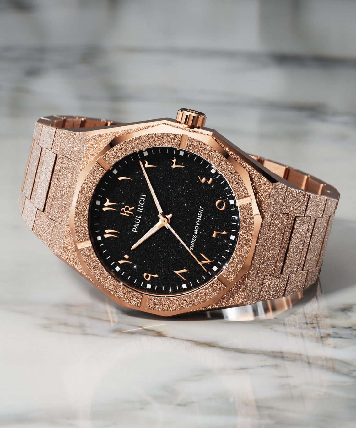 Rose gold wristwatch with a frosted textured case and bracelet, black aventurine dial, and Arabic numerals, displayed on a white marble surface. Rose gold wristwatch with a frosted textured case and bracelet, black aventurine dial, and Arabic numerals, displayed on a white marble surface.