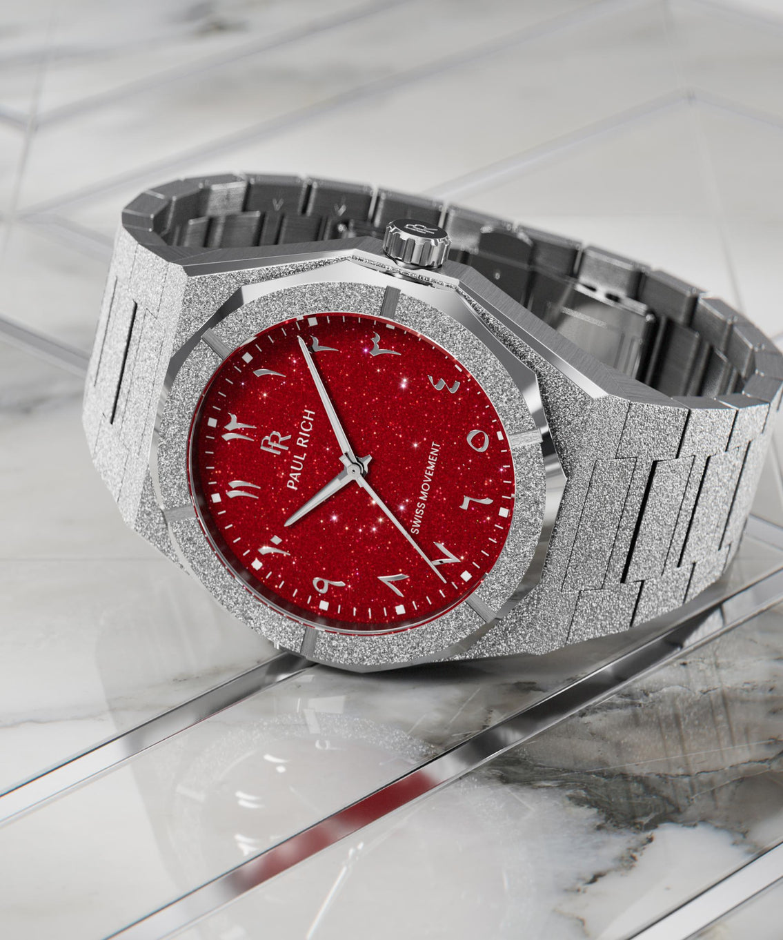 Paul Rich watch with frosted silver case and red aventurine dial with Arabic numerals, displayed on a polished white marble surface. Paul Rich watch with frosted silver case and red aventurine dial with Arabic numerals, displayed on a polished white marble surface.
