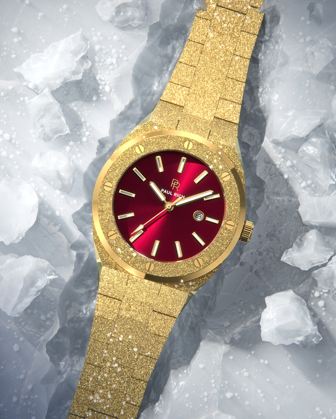 Paul Rich watch with frosted gold case and bracelet, metallic red sunray dial, and date window, displayed on a surface covered with translucent ice shards. Paul Rich watch with frosted gold case and bracelet, metallic red sunray dial, and date window, displayed on a surface covered with translucent ice shards.