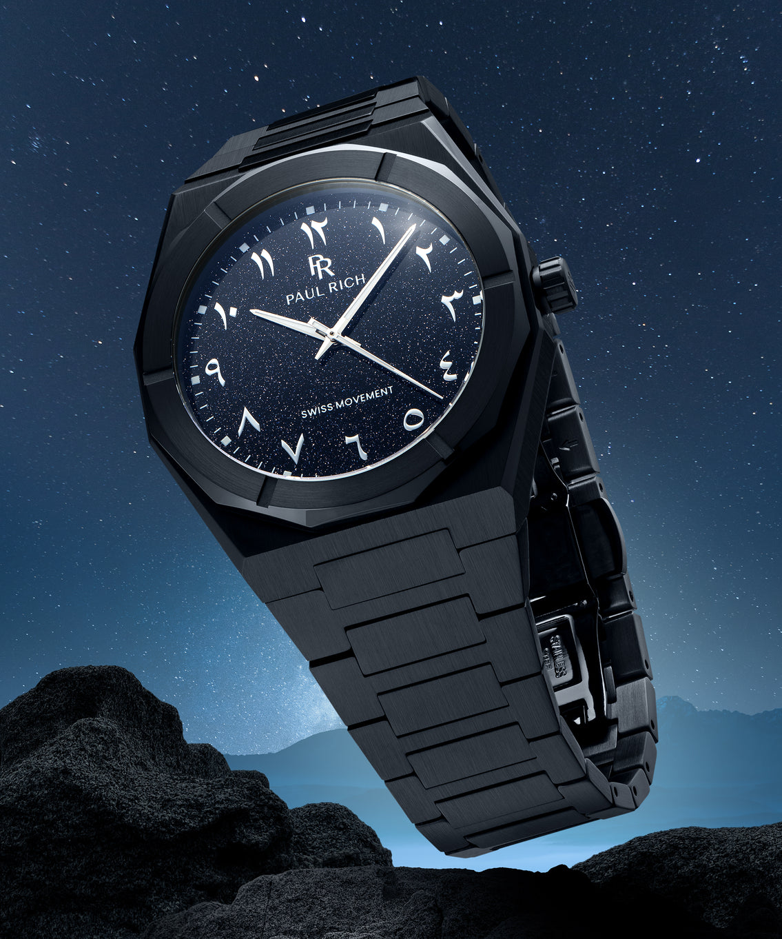 Paul Rich watch with brushed black case and blue aventurine dial with Arabic numerals, displayed above rocky terrain under a starry sky. Paul Rich watch with brushed black case and blue aventurine dial with Arabic numerals, displayed above rocky terrain under a starry sky.