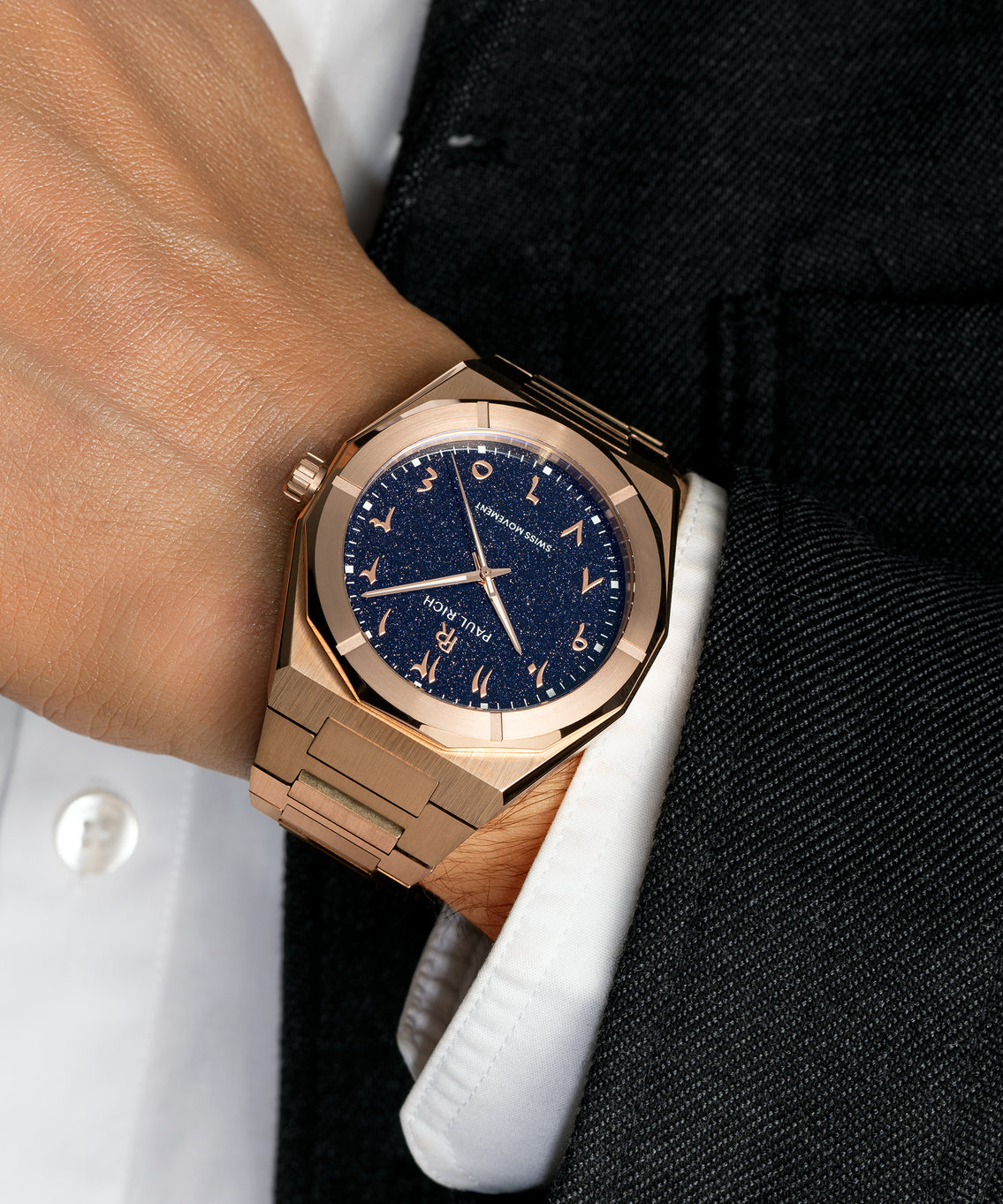 Paul Rich watch with brushed rose gold case and blue aventurine dial with Arabic numerals, worn with a white cuff and black suit. Paul Rich watch with brushed rose gold case and blue aventurine dial with Arabic numerals, worn with a white cuff and black suit.