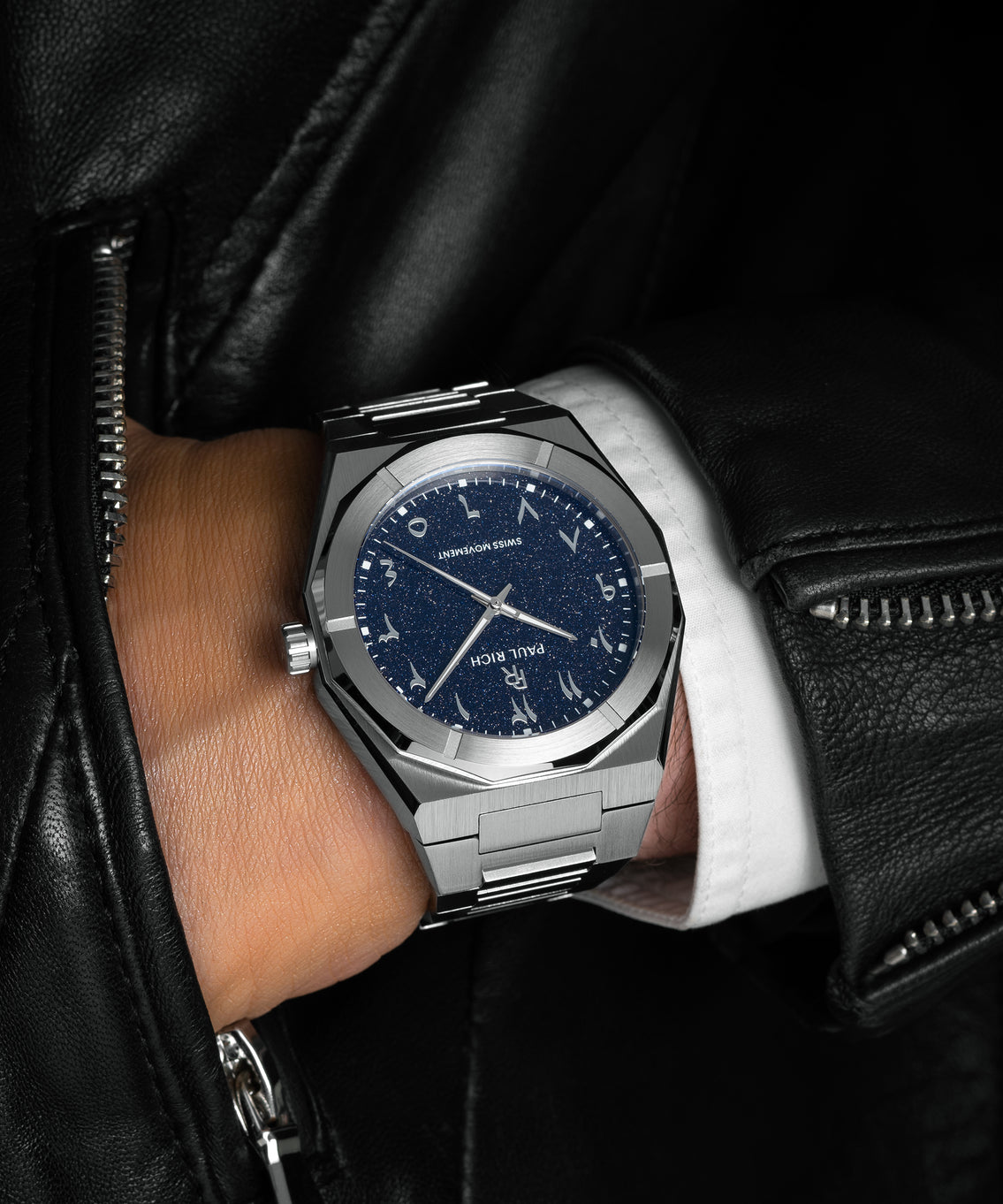 Paul Rich watch with brushed silver case and blue aventurine dial with Arabic numerals, worn with a white cuff and black leather jacket. Paul Rich watch with brushed silver case and blue aventurine dial with Arabic numerals, worn with a white cuff and black leather jacket.