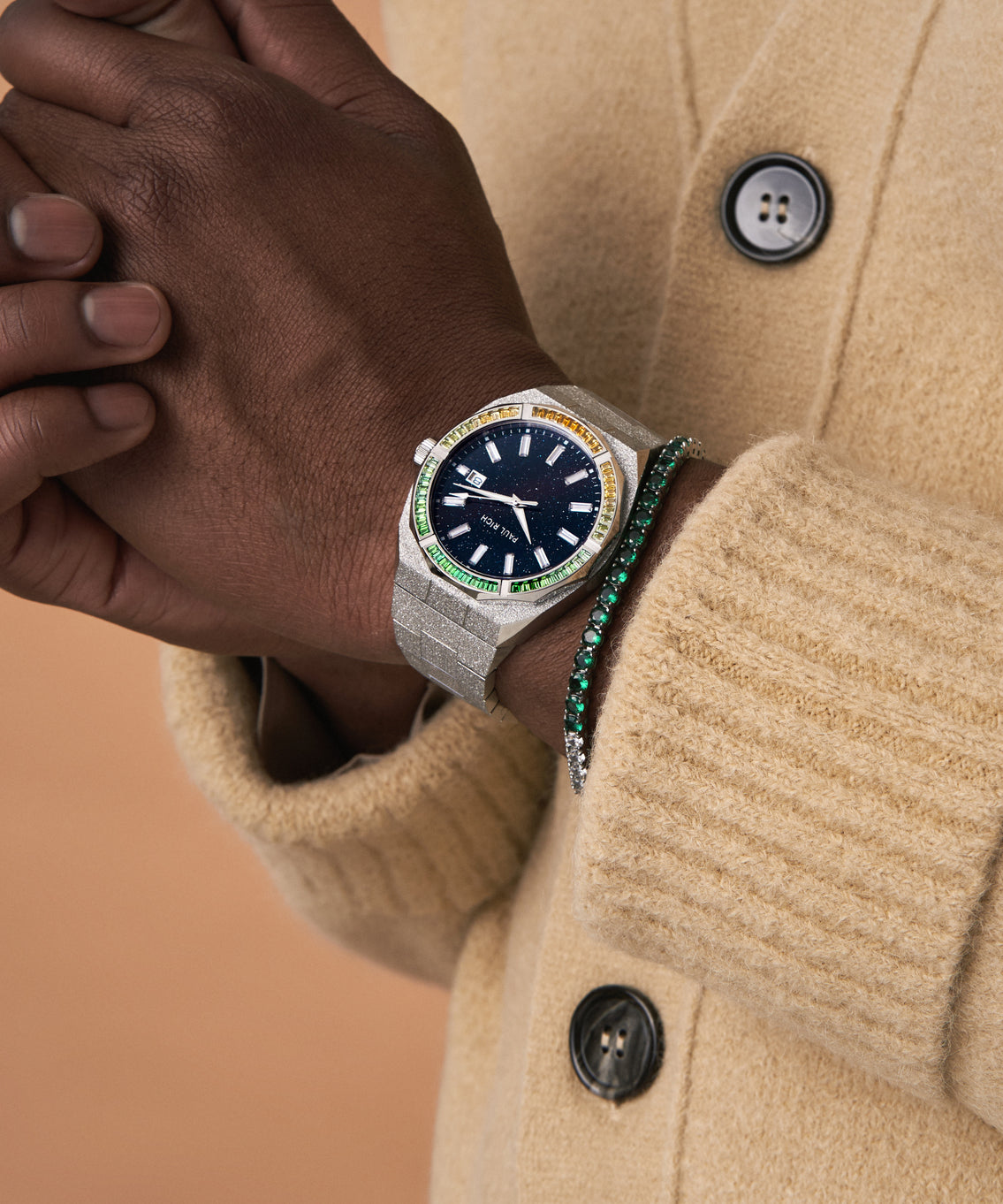 Man wearing a silver frosted Paul Rich watch with blue aventurine dial and multicolor gem bezel, paired with green tennis bracelet. Man wearing a silver frosted Paul Rich watch with blue aventurine dial and multicolor gem bezel, paired with green tennis bracelet.