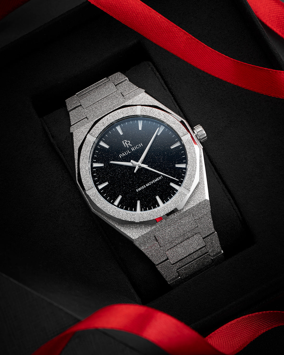 Paul Rich watch with frosted silver case and black aventurine dial, presented in a black gift box with red ribbon accents. Paul Rich watch with frosted silver case and black aventurine dial, presented in a black gift box with red ribbon accents.