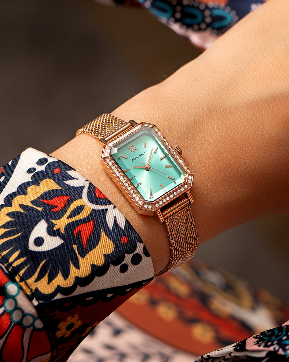 Rose gold Paul Rich watch with a mint green sunray dial, gem-set octagonal bezel, and rose gold mesh strap, worn on wrist with a colorful patterned sleeve. Rose gold Paul Rich watch with a mint green sunray dial, gem-set octagonal bezel, and rose gold mesh strap, worn on wrist with a colorful patterned sleeve.