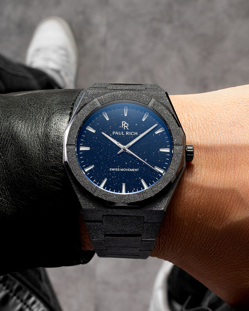 Black frosted Paul Rich watch with blue aventurine dial and silver markers, worn on wrist with black leather jacket and sneakers. Black frosted Paul Rich watch with blue aventurine dial and silver markers, worn on wrist with black leather jacket and sneakers.