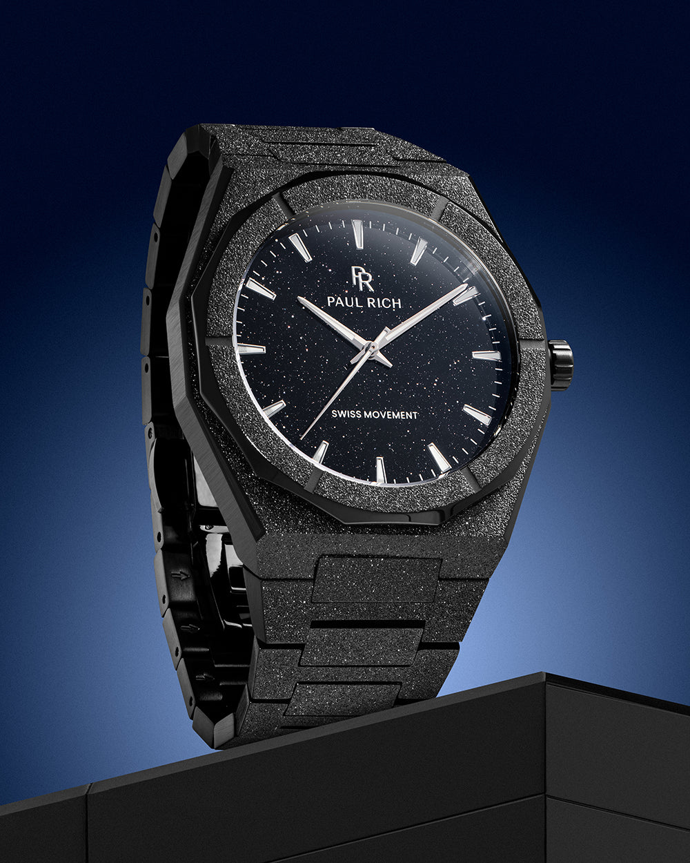 Paul Rich watch with frosted black case and black aventurine dial, displayed vertically against a blue gradient background on a black pedestal. Paul Rich watch with frosted black case and black aventurine dial, displayed vertically against a blue gradient background on a black pedestal.