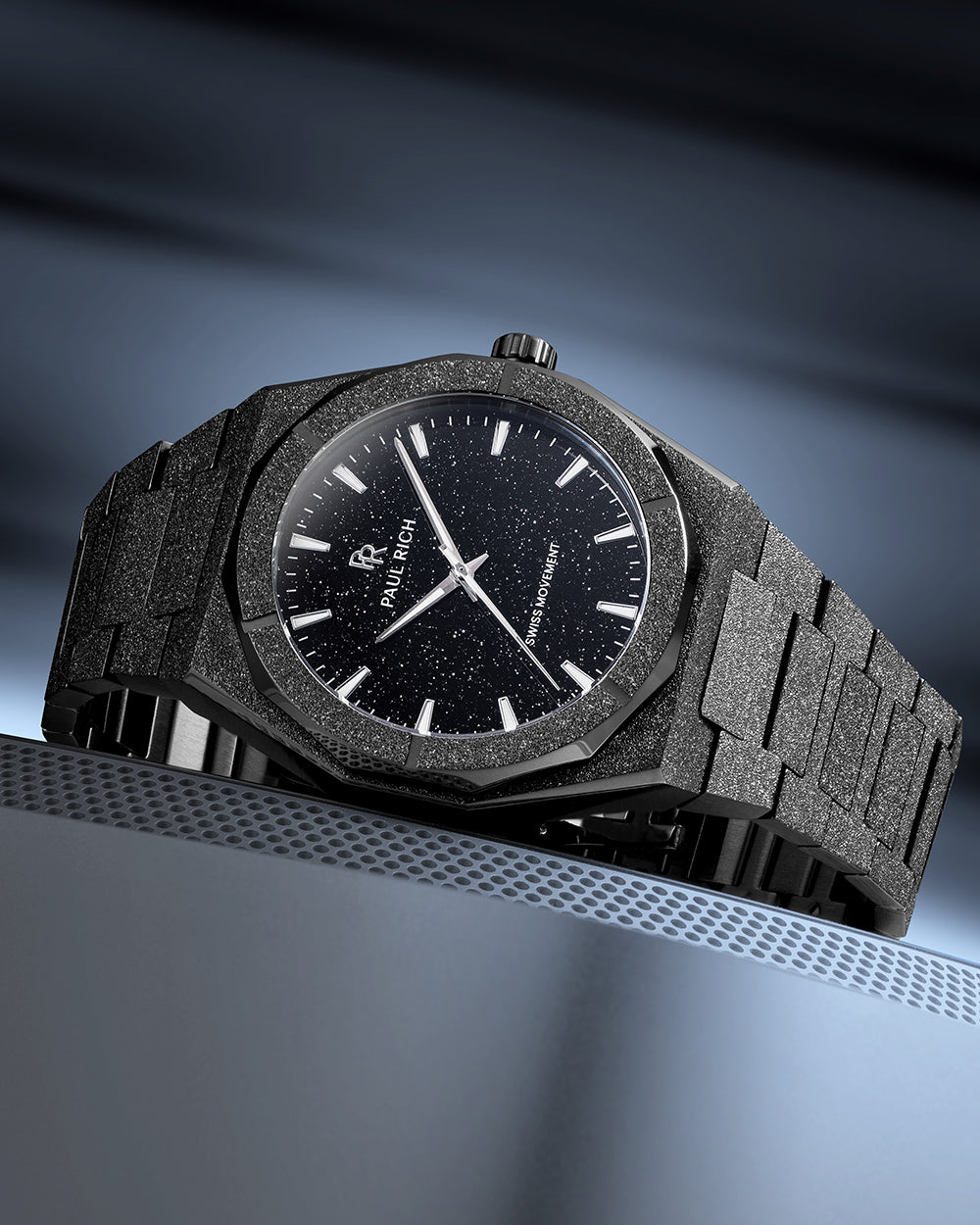 Paul Rich watch with frosted black case and black aventurine dial, displayed on a sleek metallic surface with cool blue lighting. Paul Rich watch with frosted black case and black aventurine dial, displayed on a sleek metallic surface with cool blue lighting.
