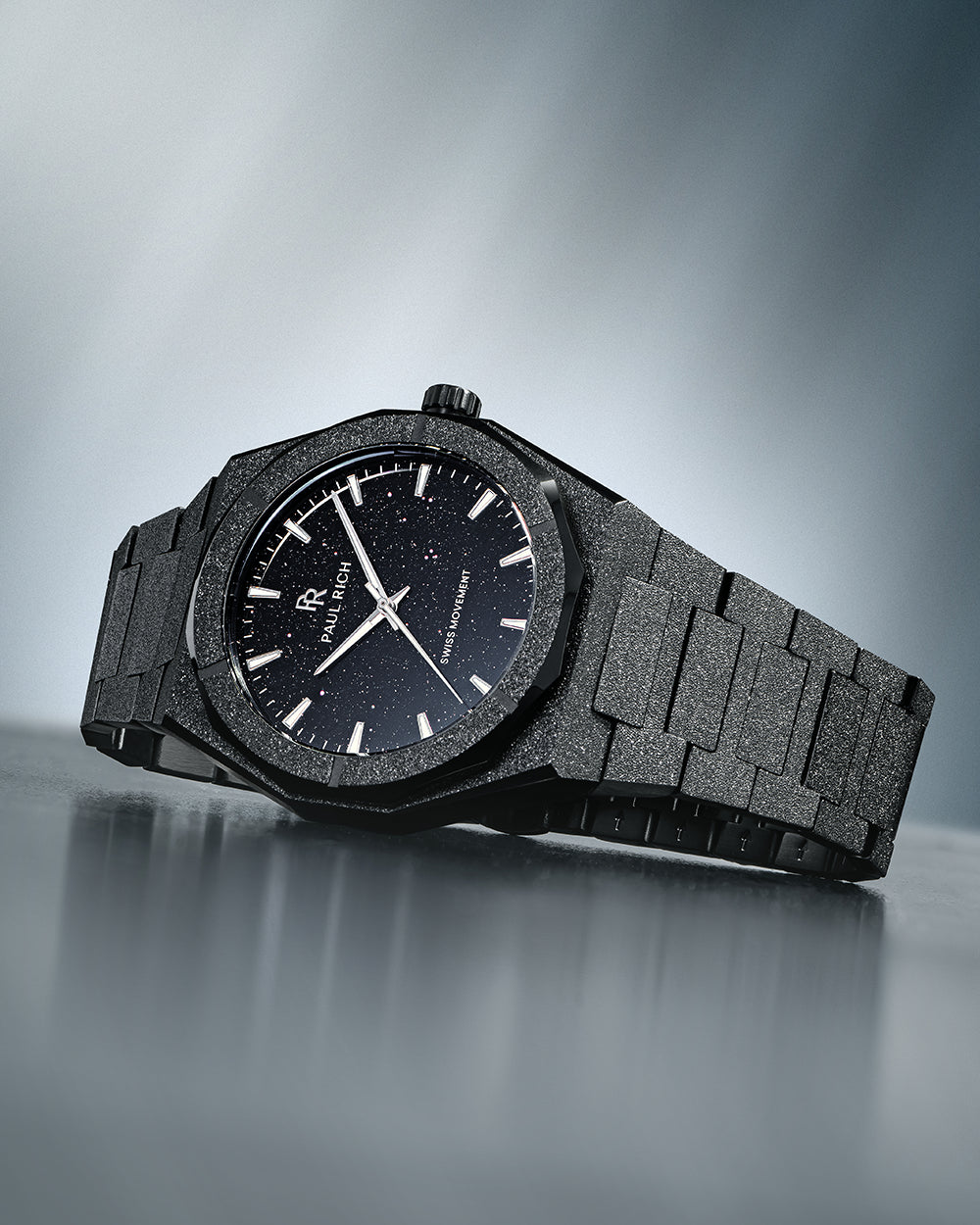 Paul Rich watch with frosted black case and black aventurine dial, resting on a reflective surface with soft gradient lighting. Paul Rich watch with frosted black case and black aventurine dial, resting on a reflective surface with soft gradient lighting.