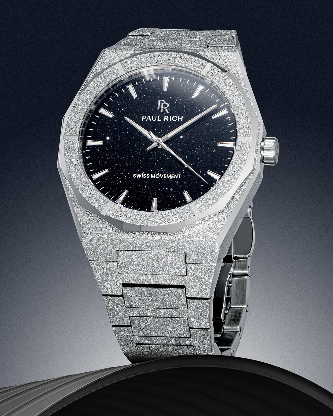 Paul Rich watch with frosted silver case and black aventurine dial, displayed vertically against a gradient background on a dark sculpted base. Paul Rich watch with frosted silver case and black aventurine dial, displayed vertically against a gradient background on a dark sculpted base.
