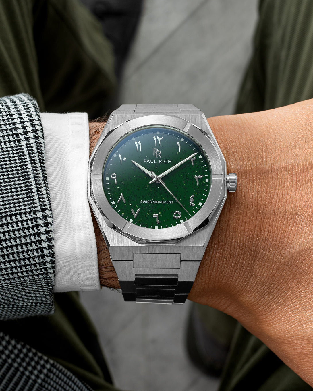 Paul Rich watch with brushed silver case and green dial featuring Arabic numerals, worn with a white cuff and houndstooth jacket. Paul Rich watch with brushed silver case and green dial featuring Arabic numerals, worn with a white cuff and houndstooth jacket.