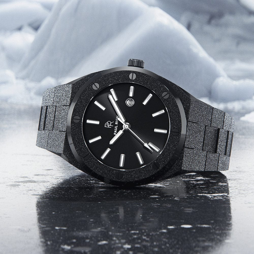 Paul Rich frosted black watch with sunray dial and silver markers, placed on icy surface with snow-covered mountains in the background. Paul Rich frosted black watch with sunray dial and silver markers, placed on icy surface with snow-covered mountains in the background.