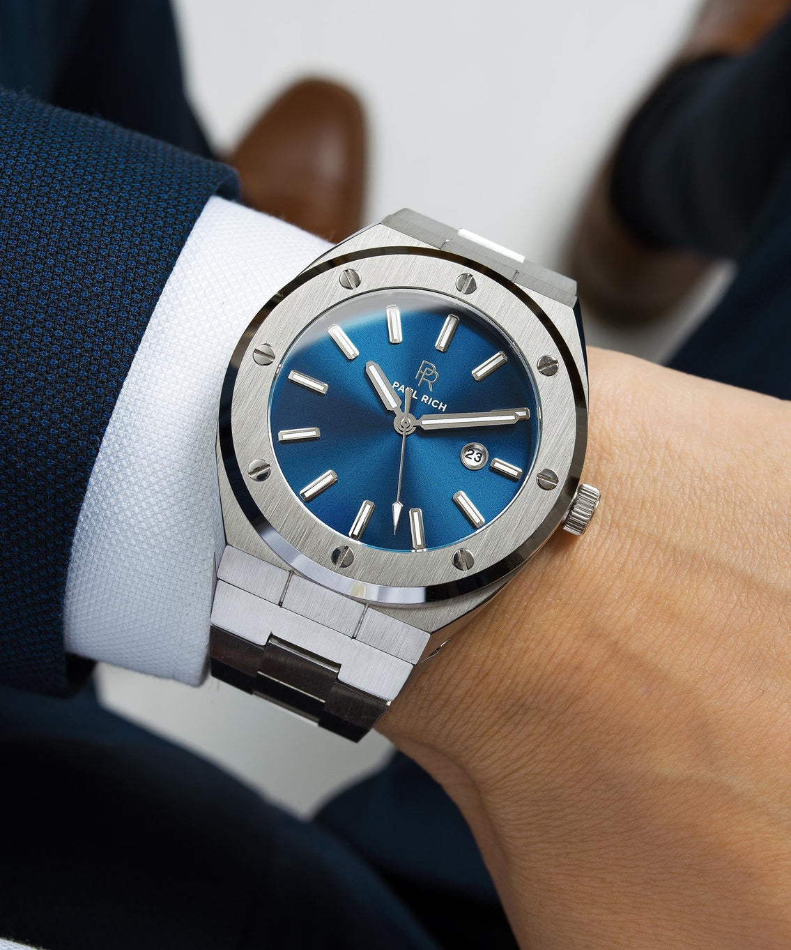 Paul Rich brushed silver watch with deep blue sunray dial and date window, worn with navy suit jacket and white shirt cuff. Paul Rich brushed silver watch with deep blue sunray dial and date window, worn with navy suit jacket and white shirt cuff.