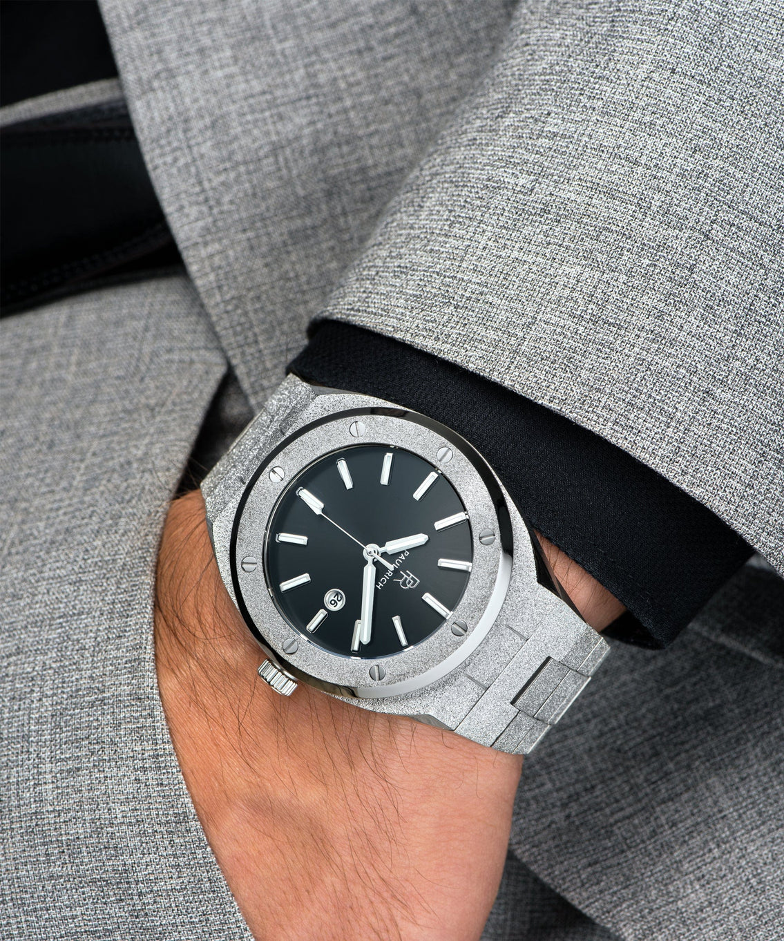 Paul Rich watch with frosted silver case and bracelet, metallic black sunray dial, and date window, worn on wrist with grey suit and black cuff. Paul Rich watch with frosted silver case and bracelet, metallic black sunray dial, and date window, worn on wrist with grey suit and black cuff.