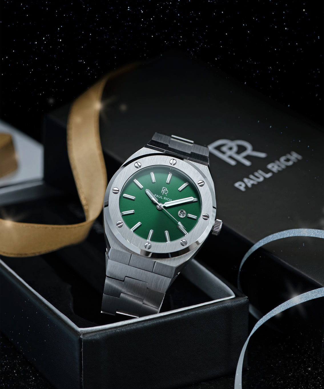 Paul Rich brushed silver watch with green dial and date window, displayed in open gift box with gold ribbon and starry night background. Paul Rich brushed silver watch with green dial and date window, displayed in open gift box with gold ribbon and starry night background.